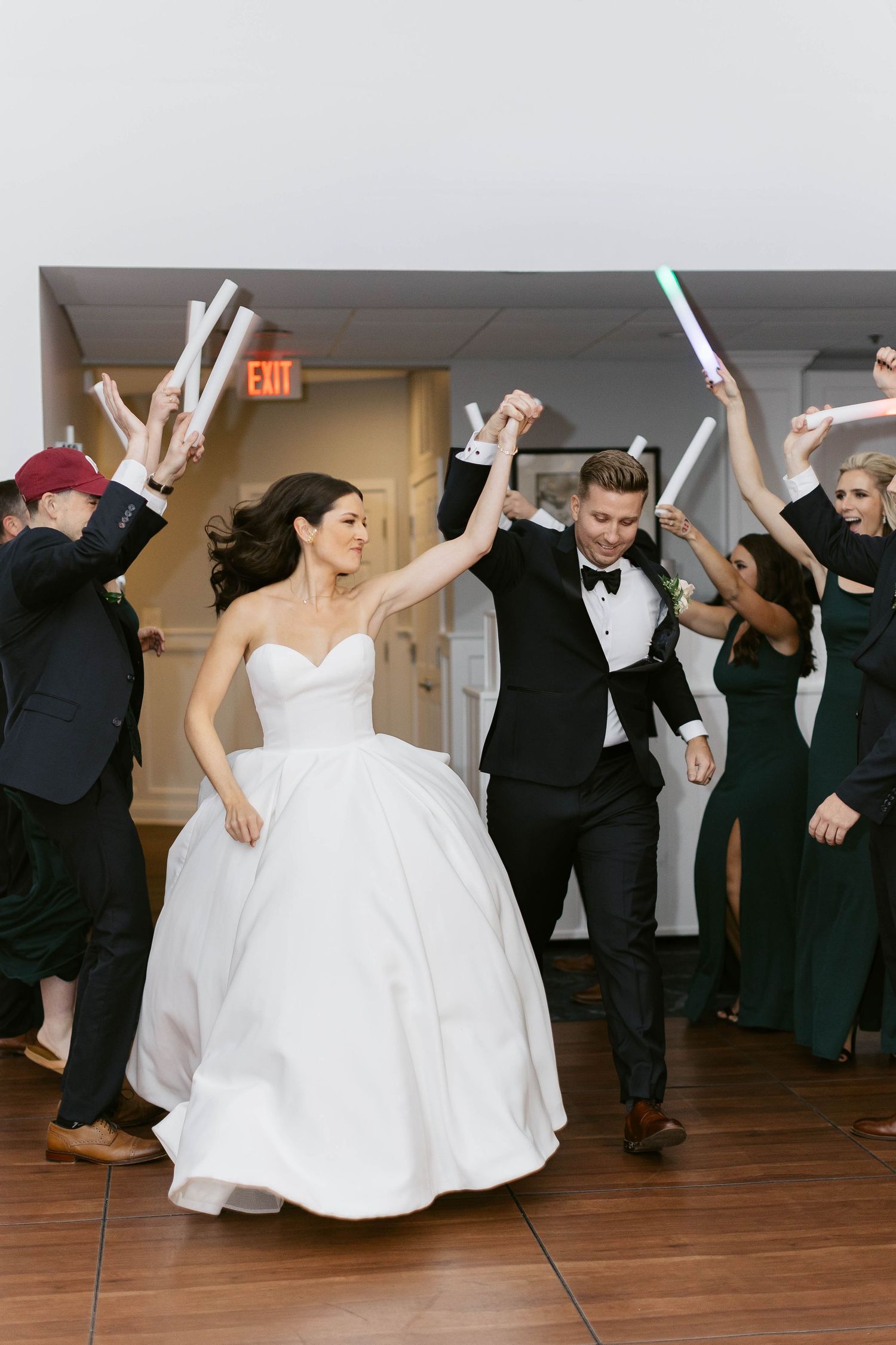 Wedding party dances energetically on wooden dance floor during reception celebration.