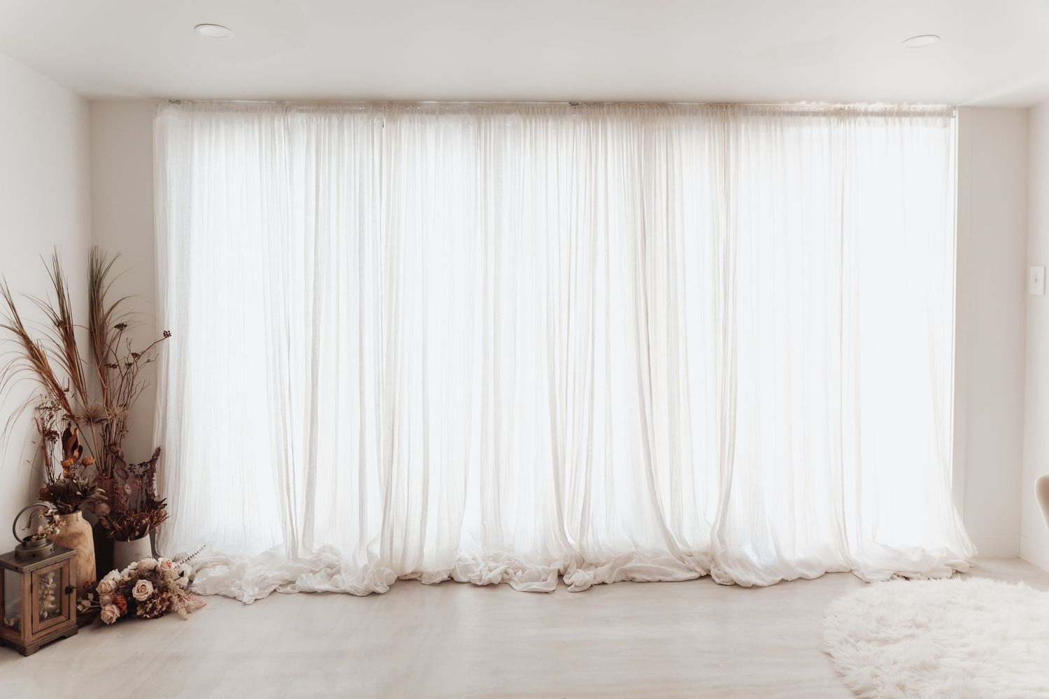 A bright white studio space with sheer curtains covering windows and a wooden accent piece in the corner.
