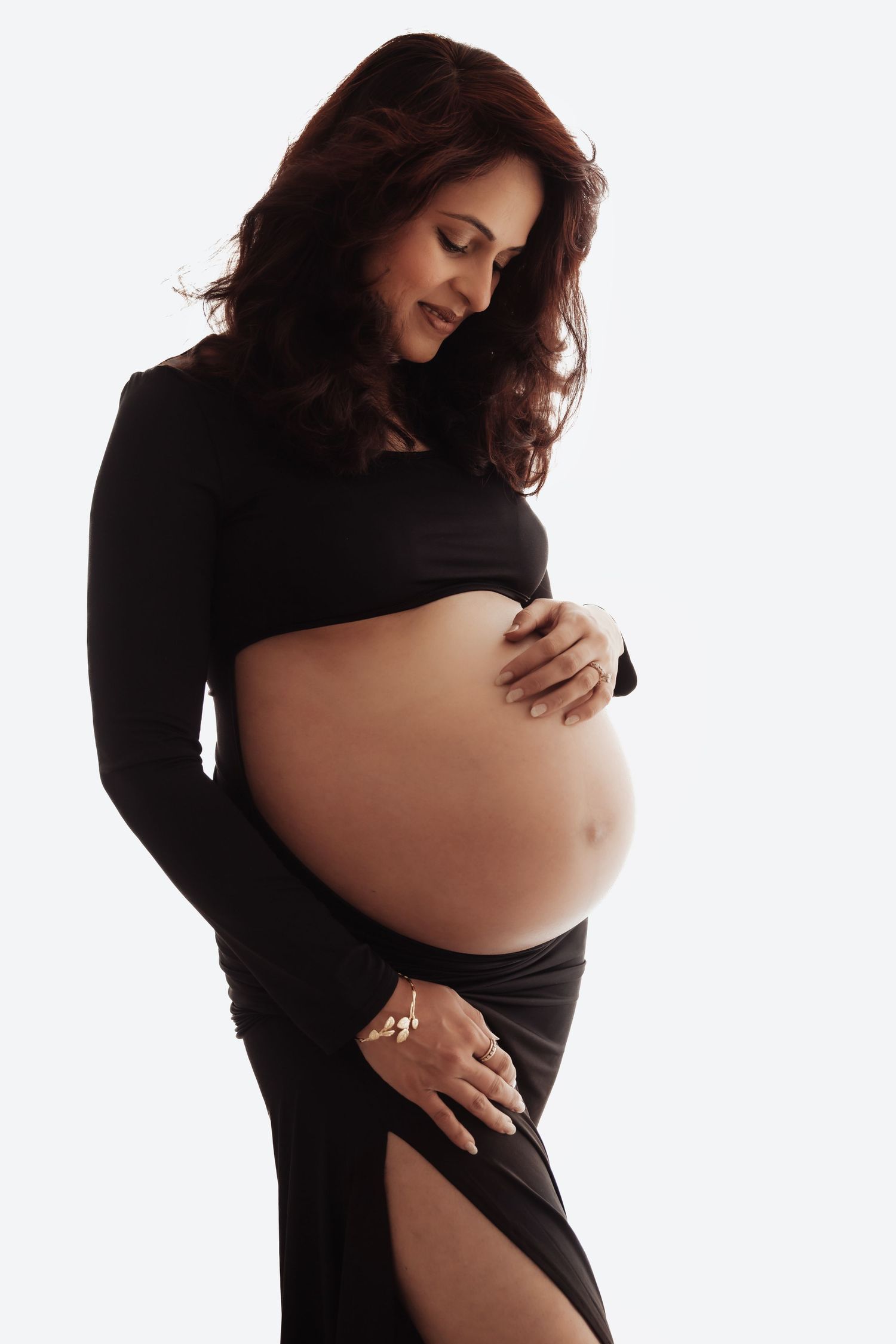 Pregnant woman in black outfit cradling her baby bump, showcasing maternity fashion on white background.