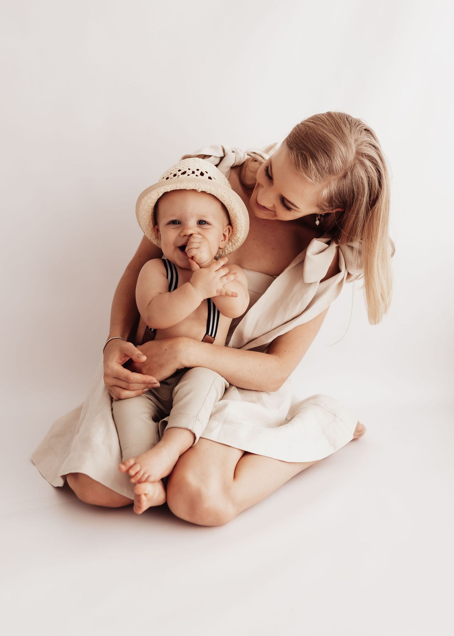 A tender moment captured in soft beige tones as mother and baby in white attire share an intimate embrace.