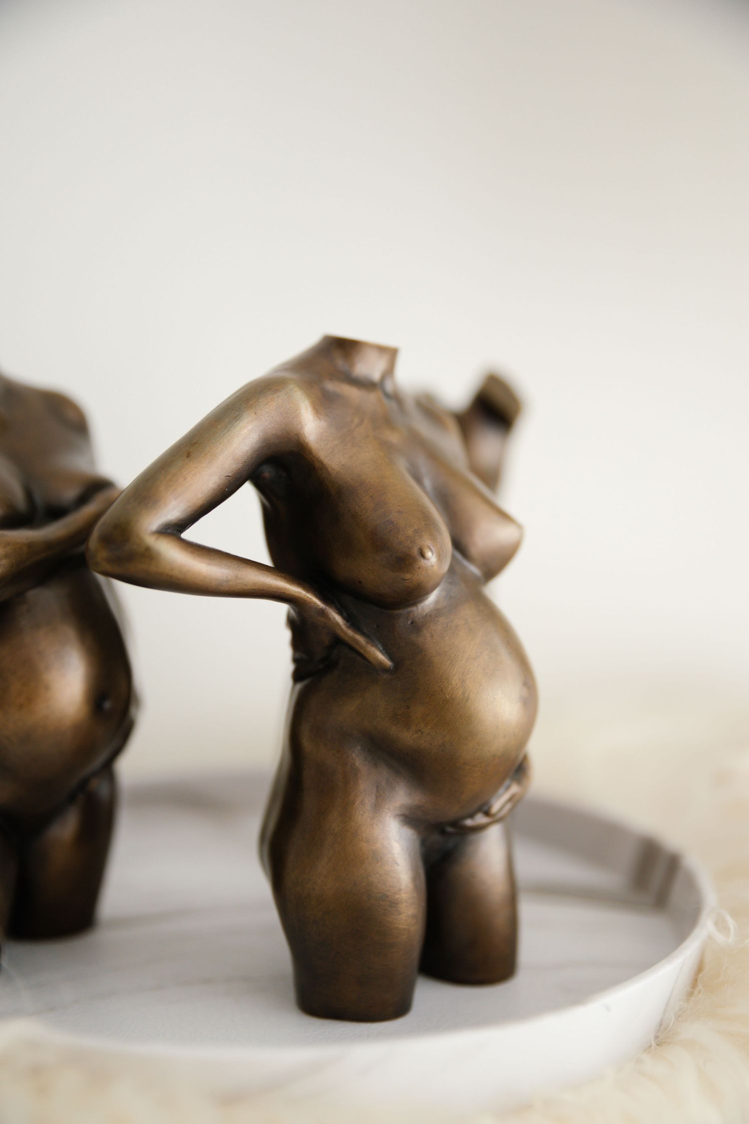 Bronze sculpture of a headless pregnant female figure kneeling on a white plate, showcasing maternal beauty.