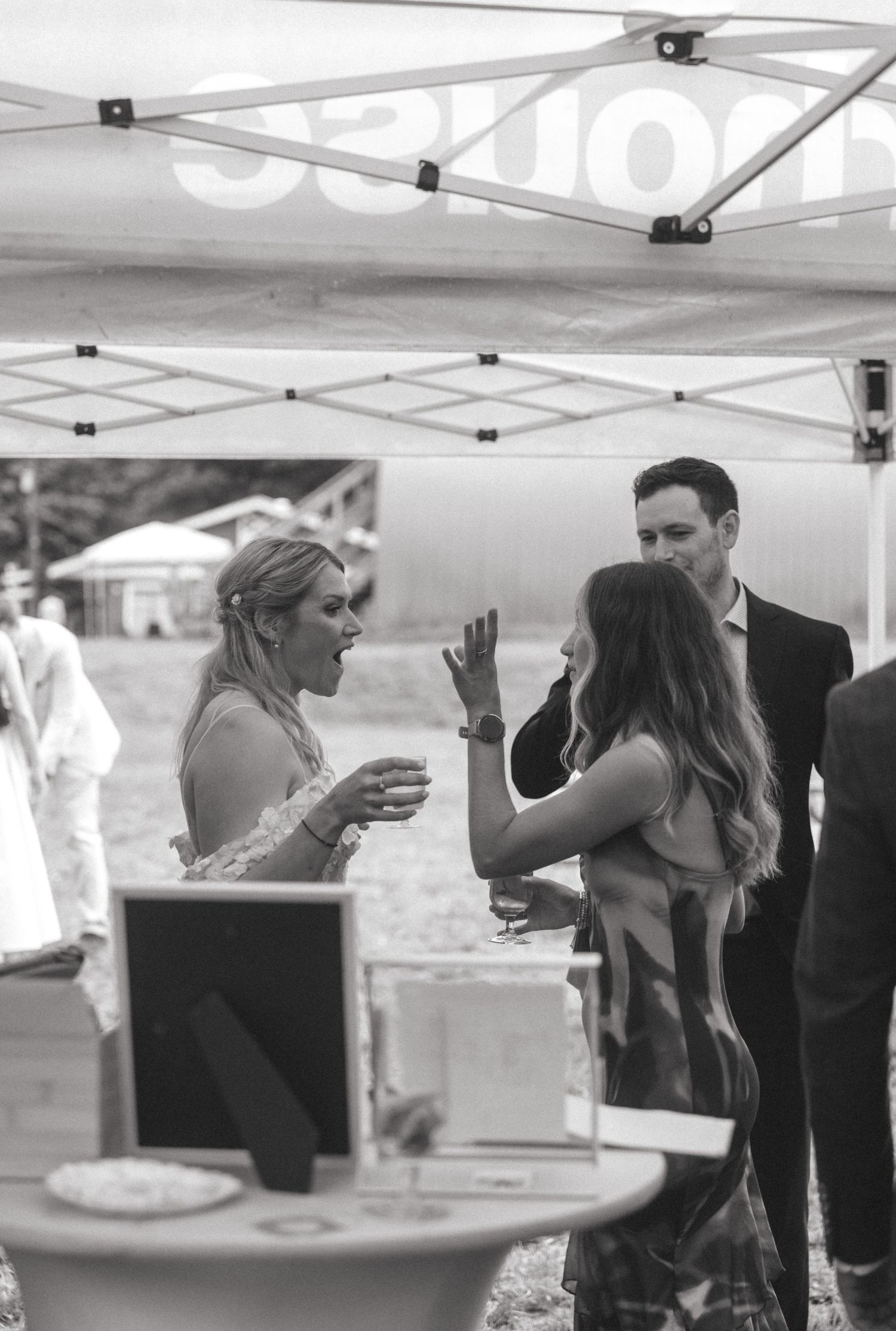 Wedding reception guests gathering under a white canopy tent.