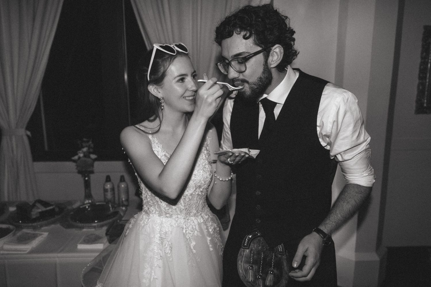 A couple sharing cake during their wedding reception in black and white.