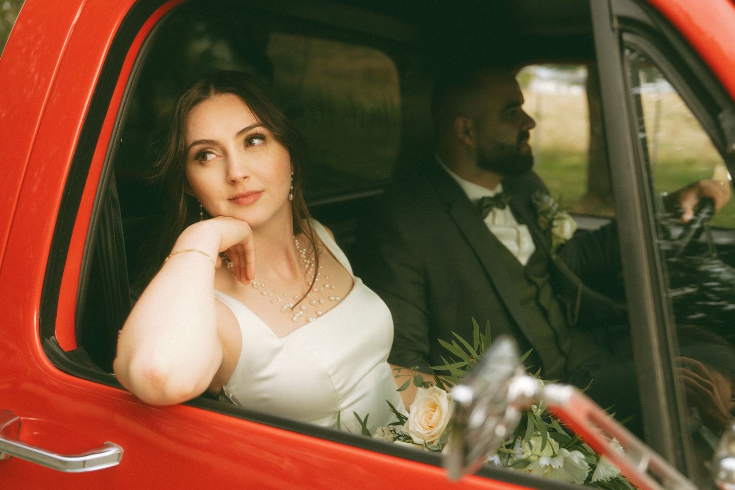 Bride and groom seated in vintage red car during wedding portraits.