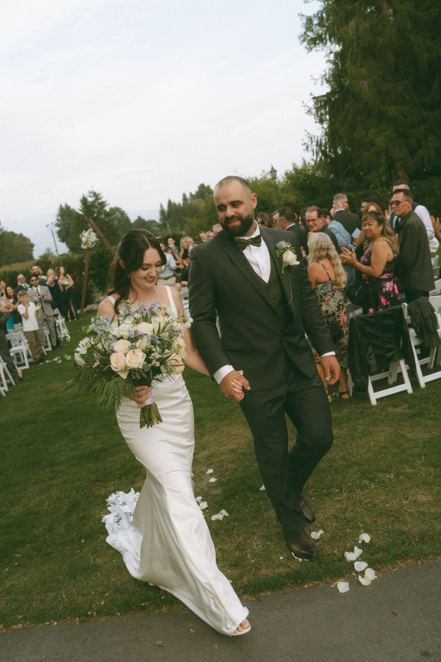 Newlyweds share a romantic dance moment on a paved pathway surrounded by wedding guests.