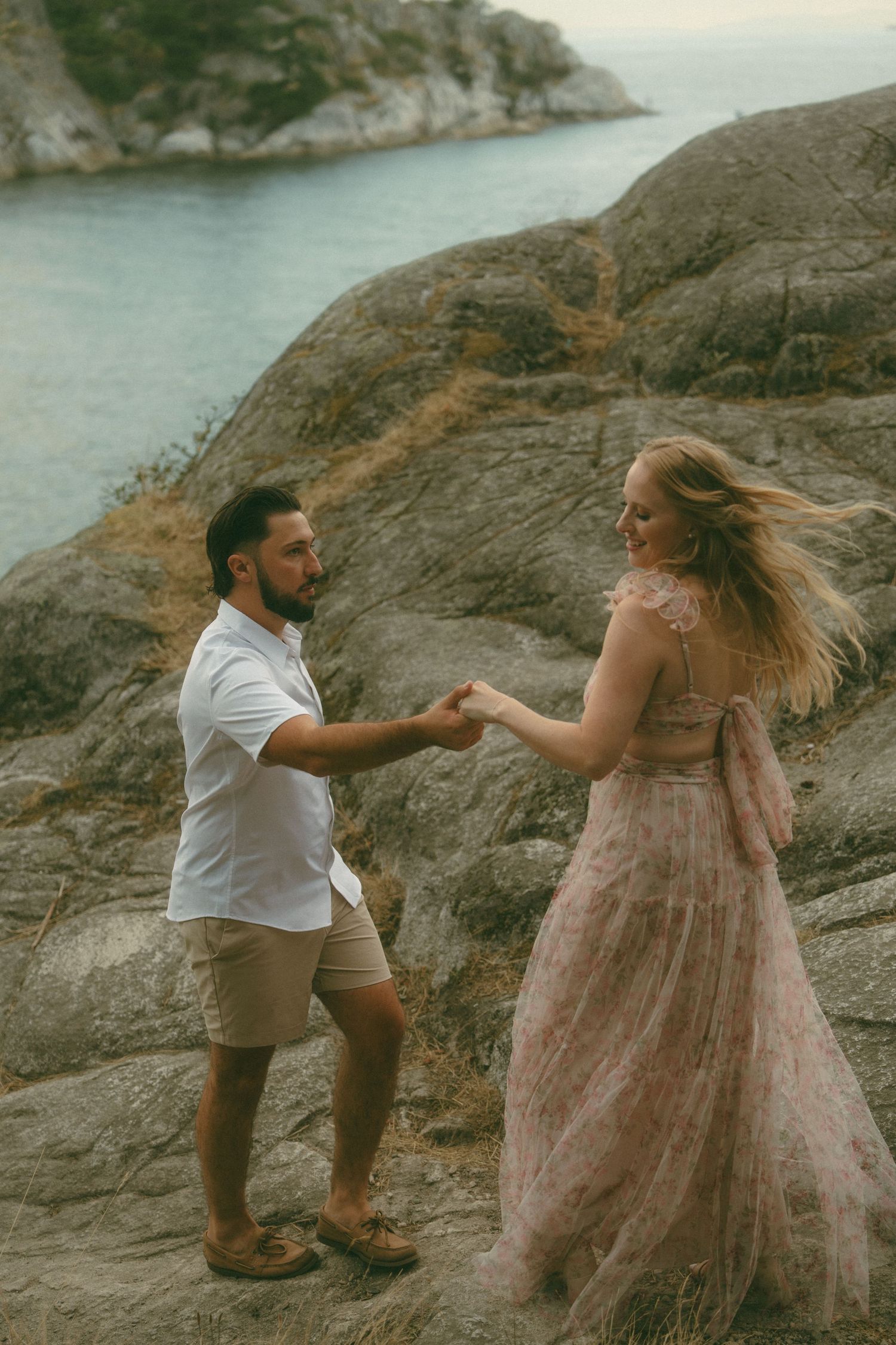 Couple shares romantic moments on rocky coastal cliffs at sunset.