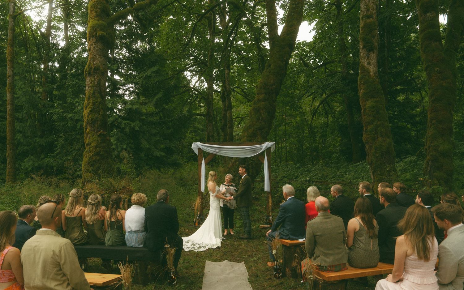 Outdoor wedding ceremony setup with wooden chairs in a wooded forest setting.