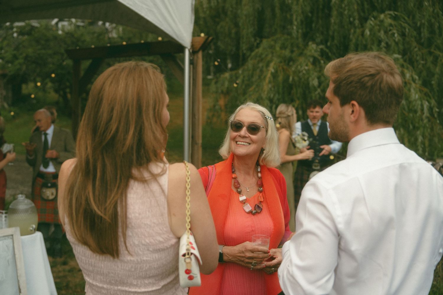 Guests mingling at an outdoor wedding reception with white tent and mountain scenery.