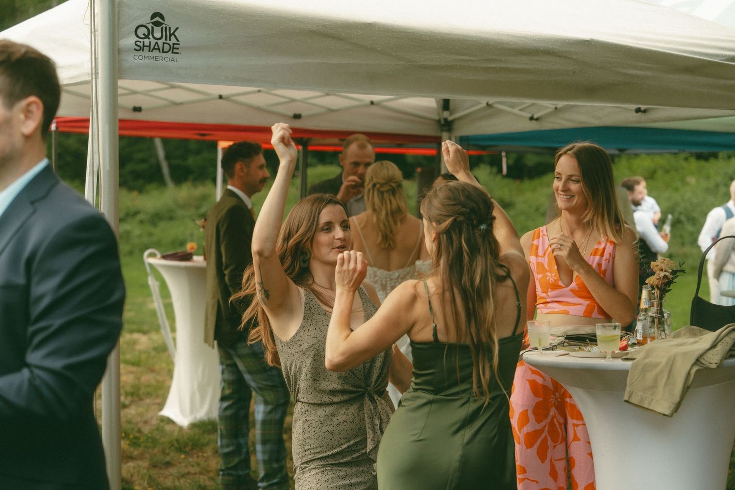 Wedding guests enjoying refreshments and conversation under a white tent.