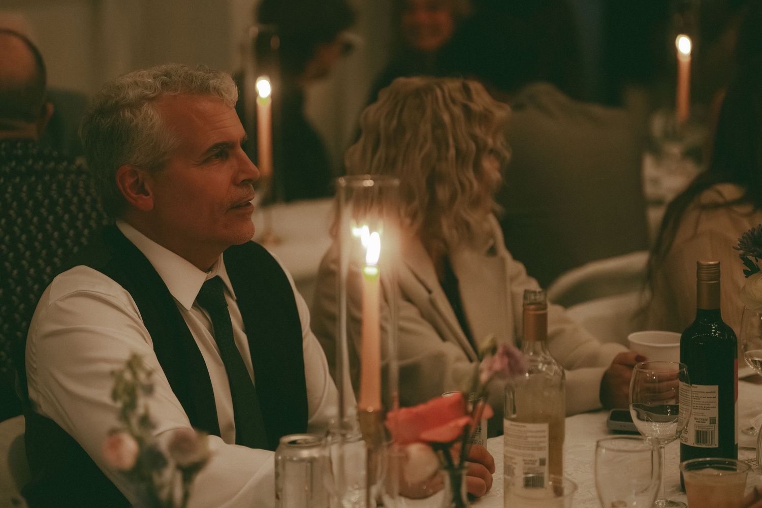 Candlelit wedding reception dinner with guests seated at tables with wine bottles.