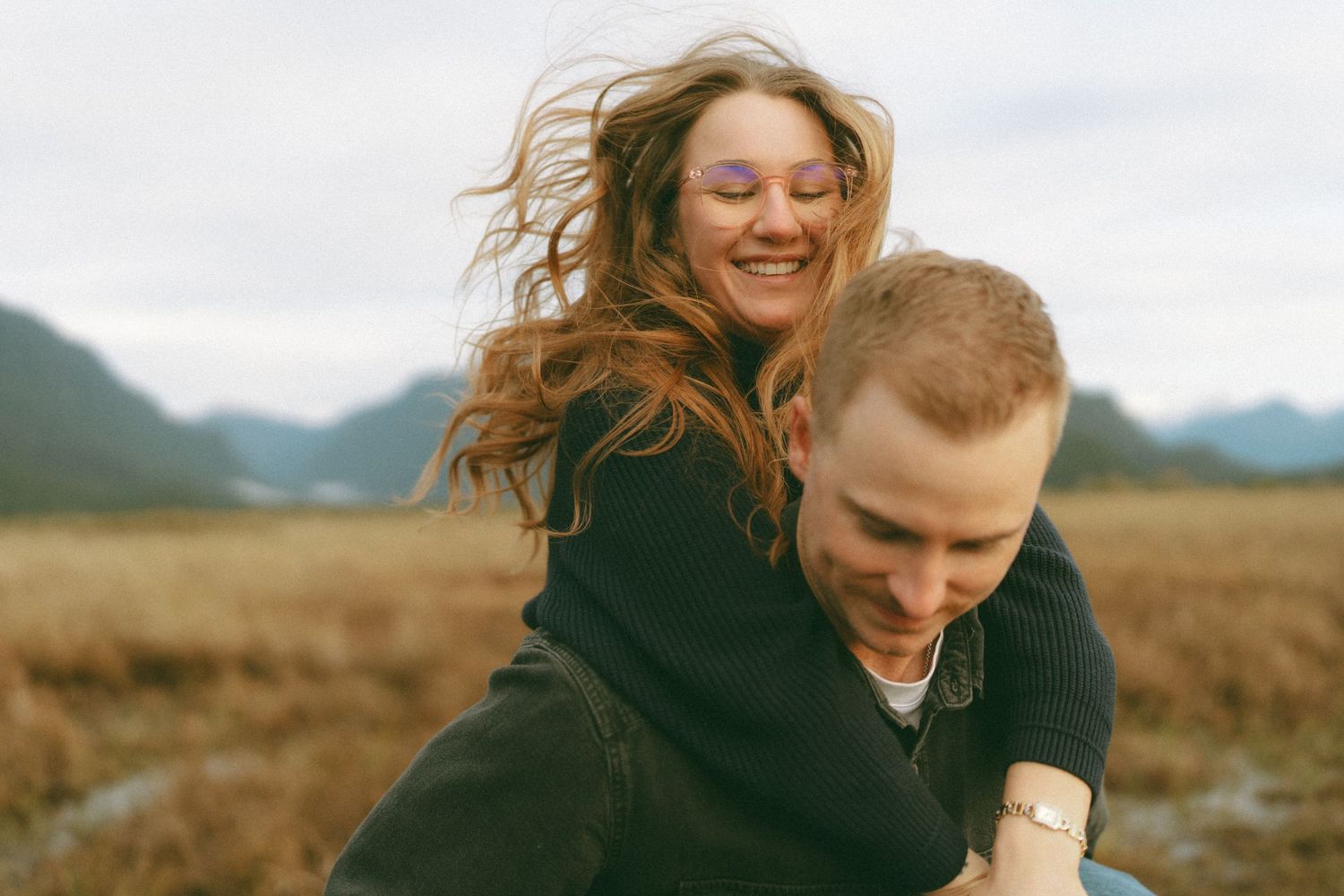 Couple sharing intimate moments in an autumn field with mountains in background.