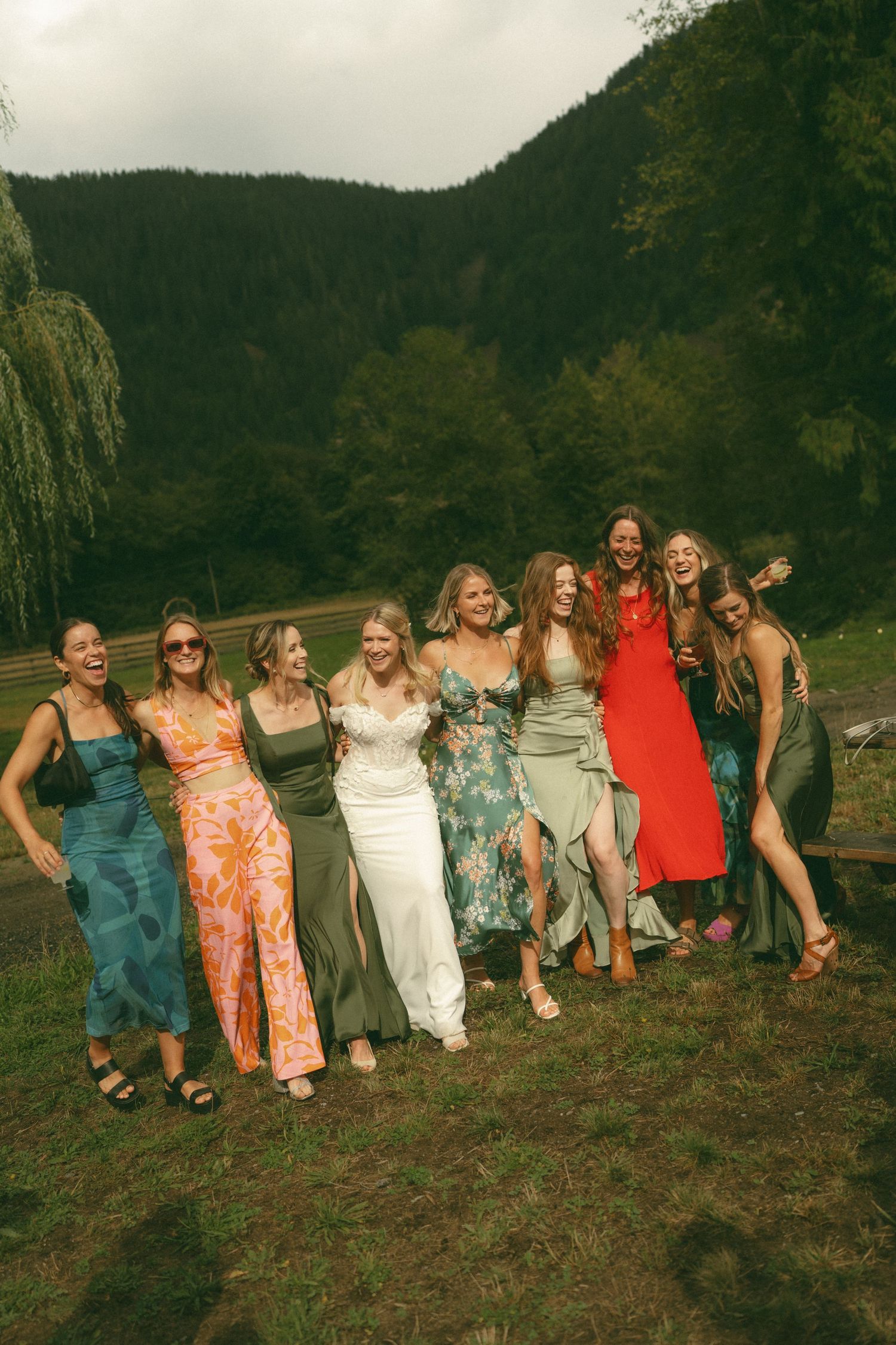 Group photo of wedding party members posing together on a hillside with mountain backdrop.