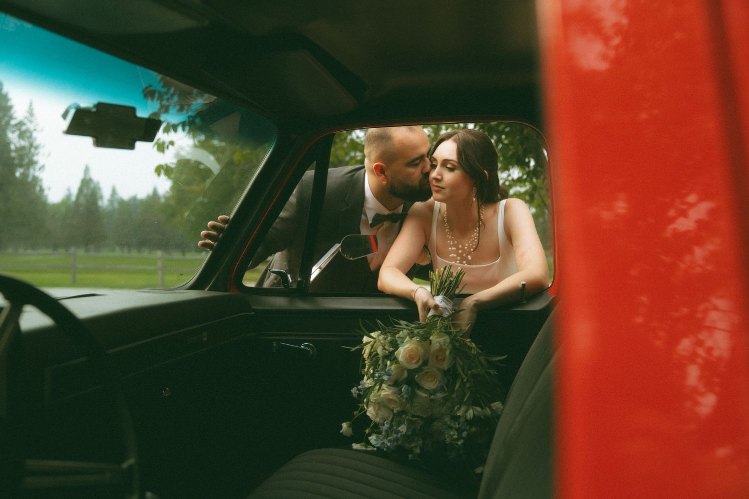 Classic red car serves as backdrop for romantic wedding photography.