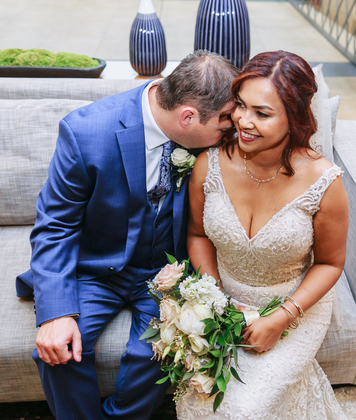 Wedding couple in blue suit and sparkly dress sharing intimate moment with bouquet.