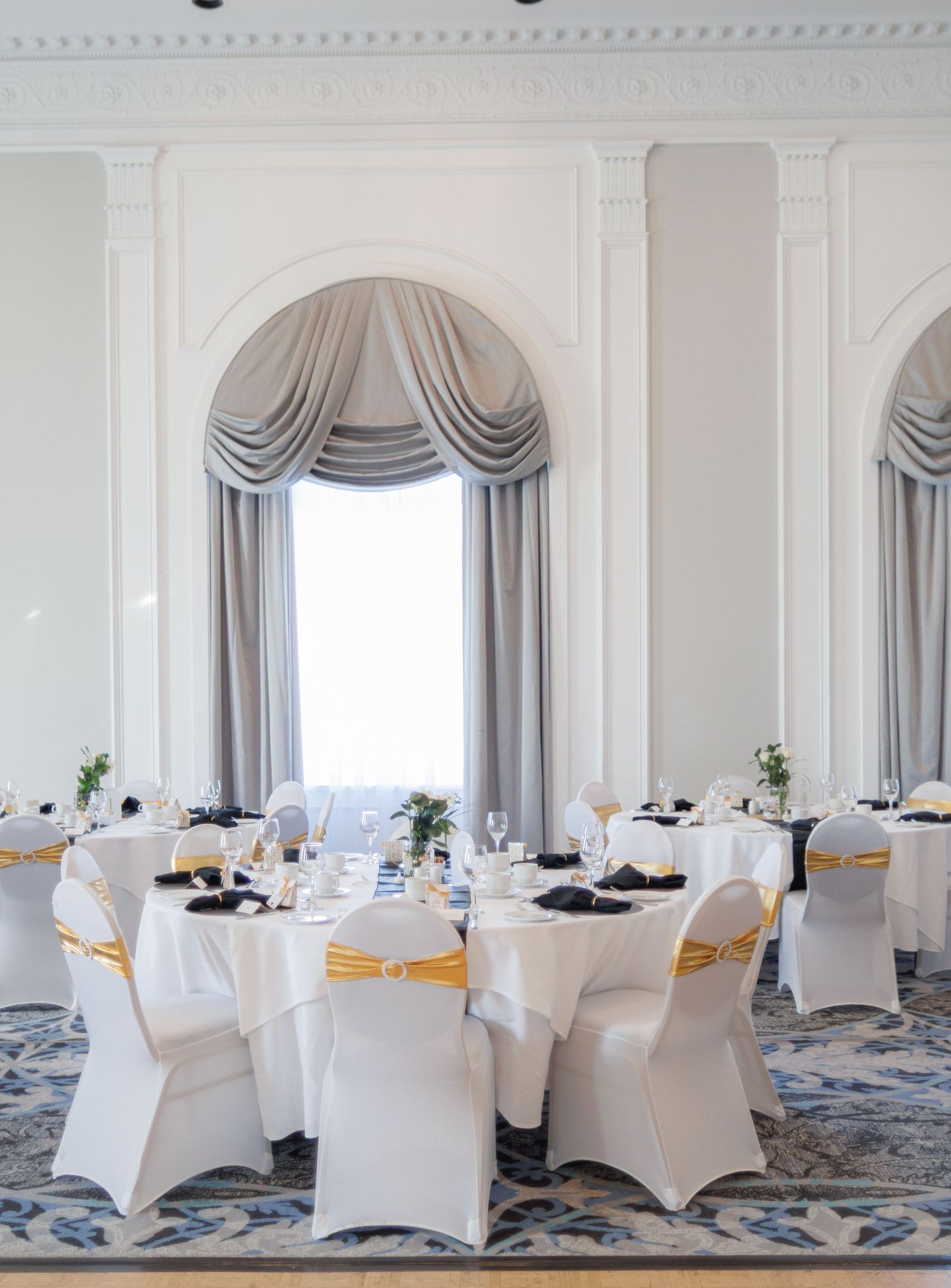 Wedding reception room with white spandex chair covers and gold sashes in an elegant ballroom.