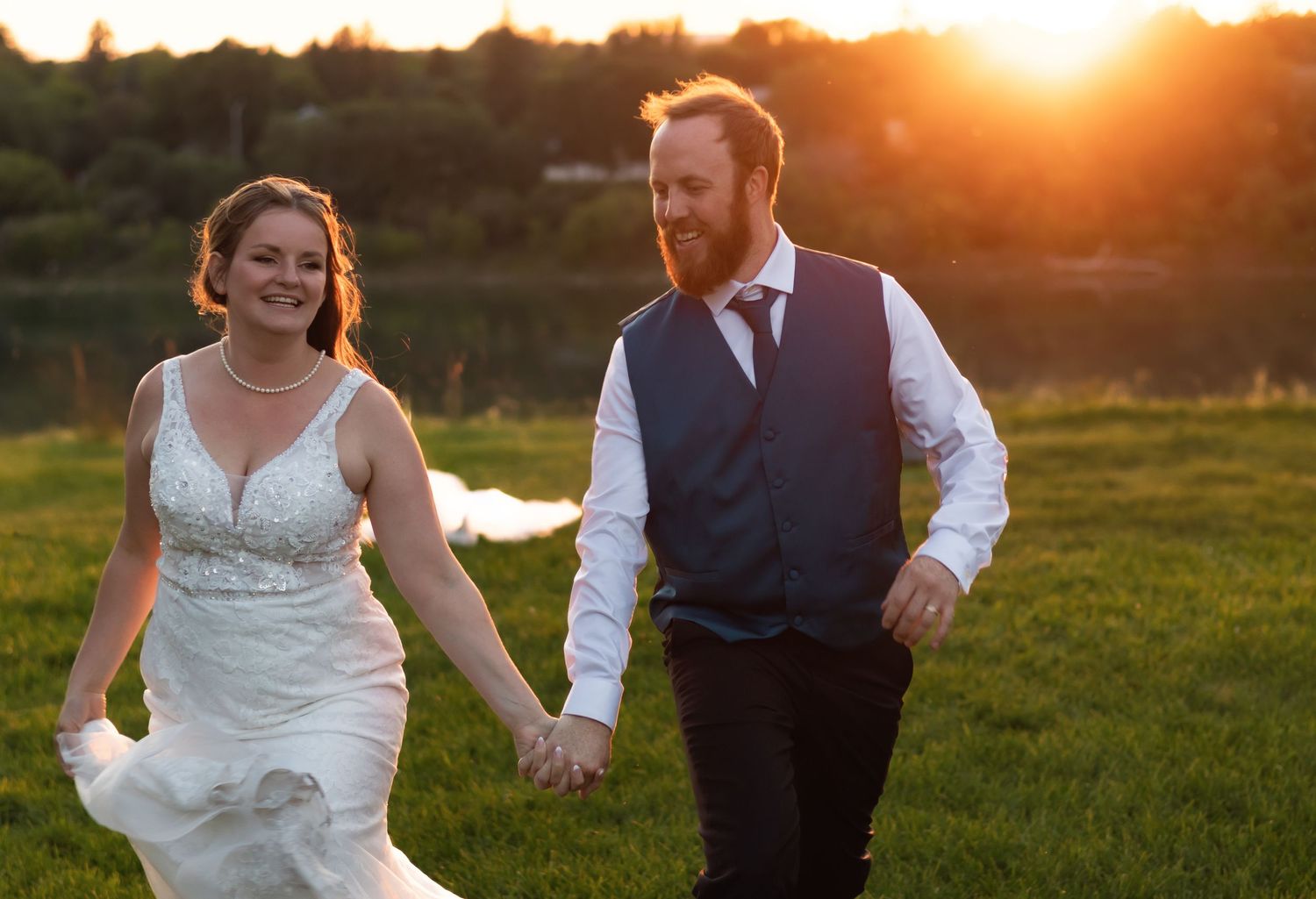 Joyful newlyweds dance and celebrate in a sunlit field at golden hour.
