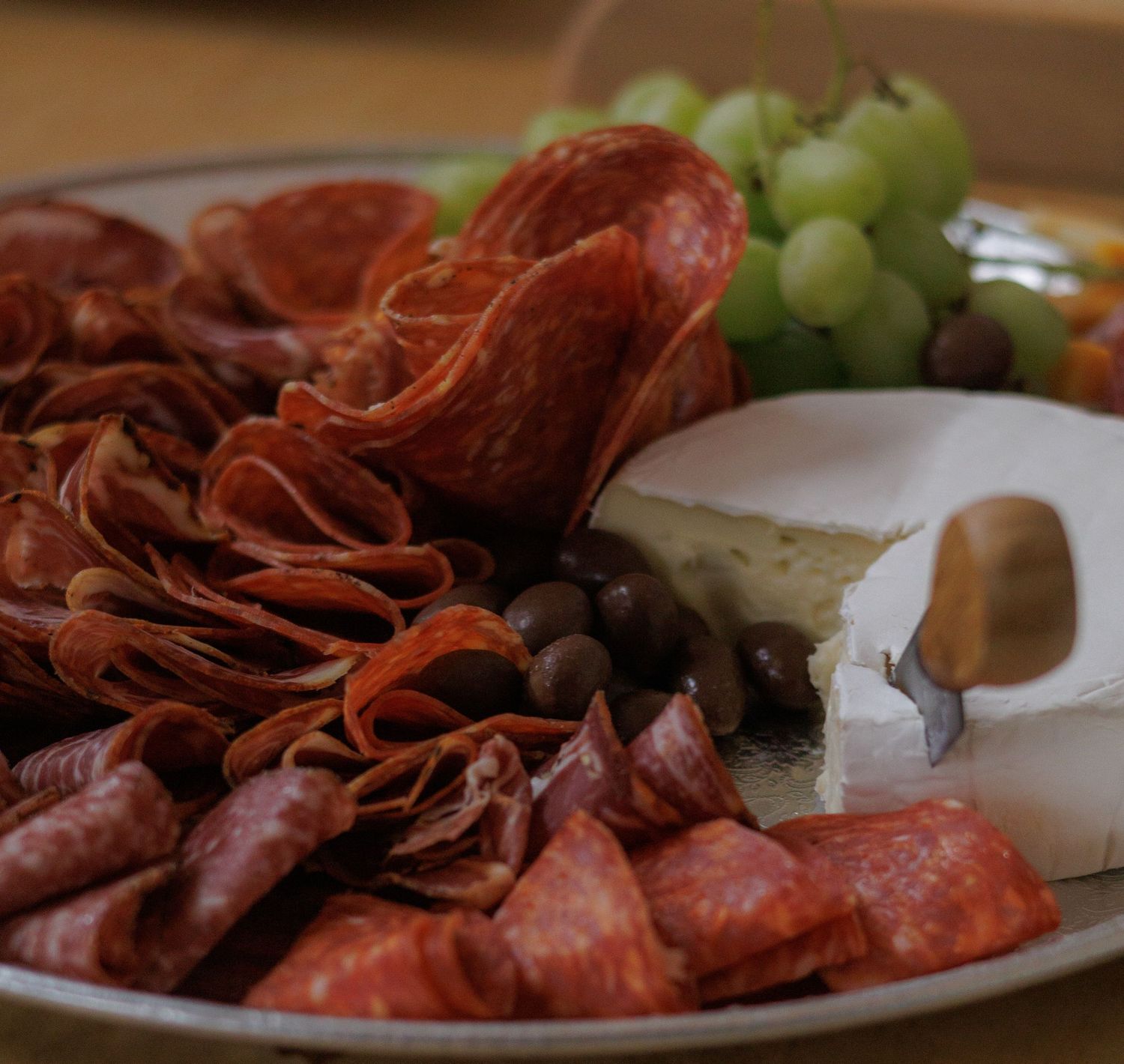 Charcuterie board with assorted meats, grapes, and snacks arranged on a white platter.