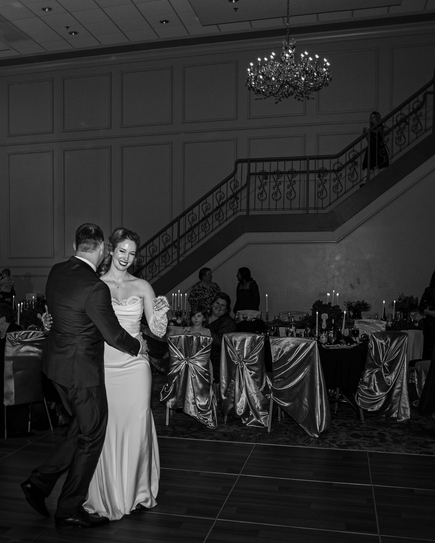 Romantic dance scene in an elegant ballroom with dramatic lighting and chandelier overhead.