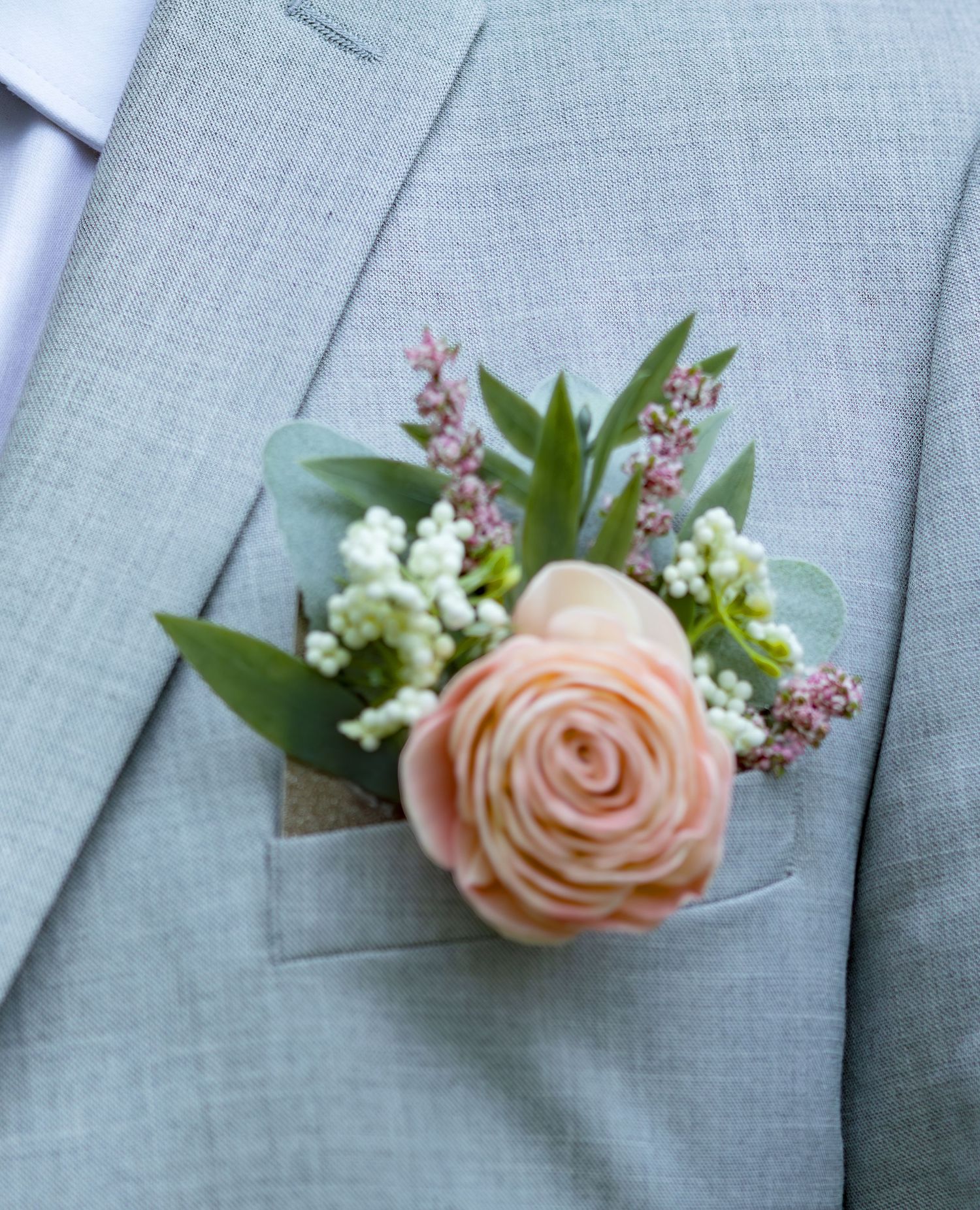 Peach rose boutonnieres with small white flowers pinned to light gray suit jackets.