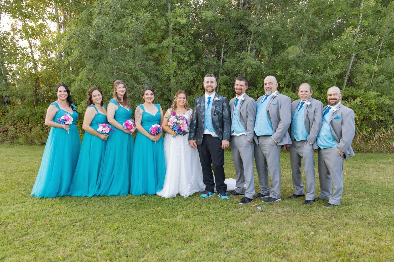 Wedding party in turquoise and gray attire posed together outdoors.