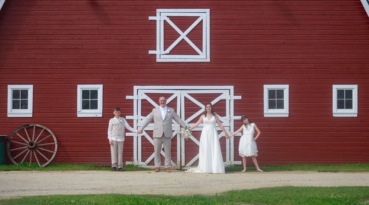 Wedding party poses in front of a classic red barn with white trim.