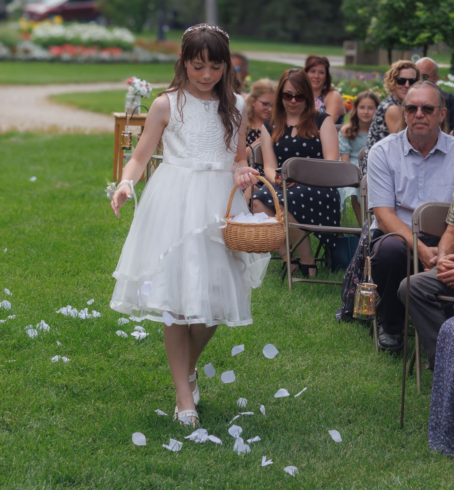 Flower girl walking down outdoor aisle with scattered petals.