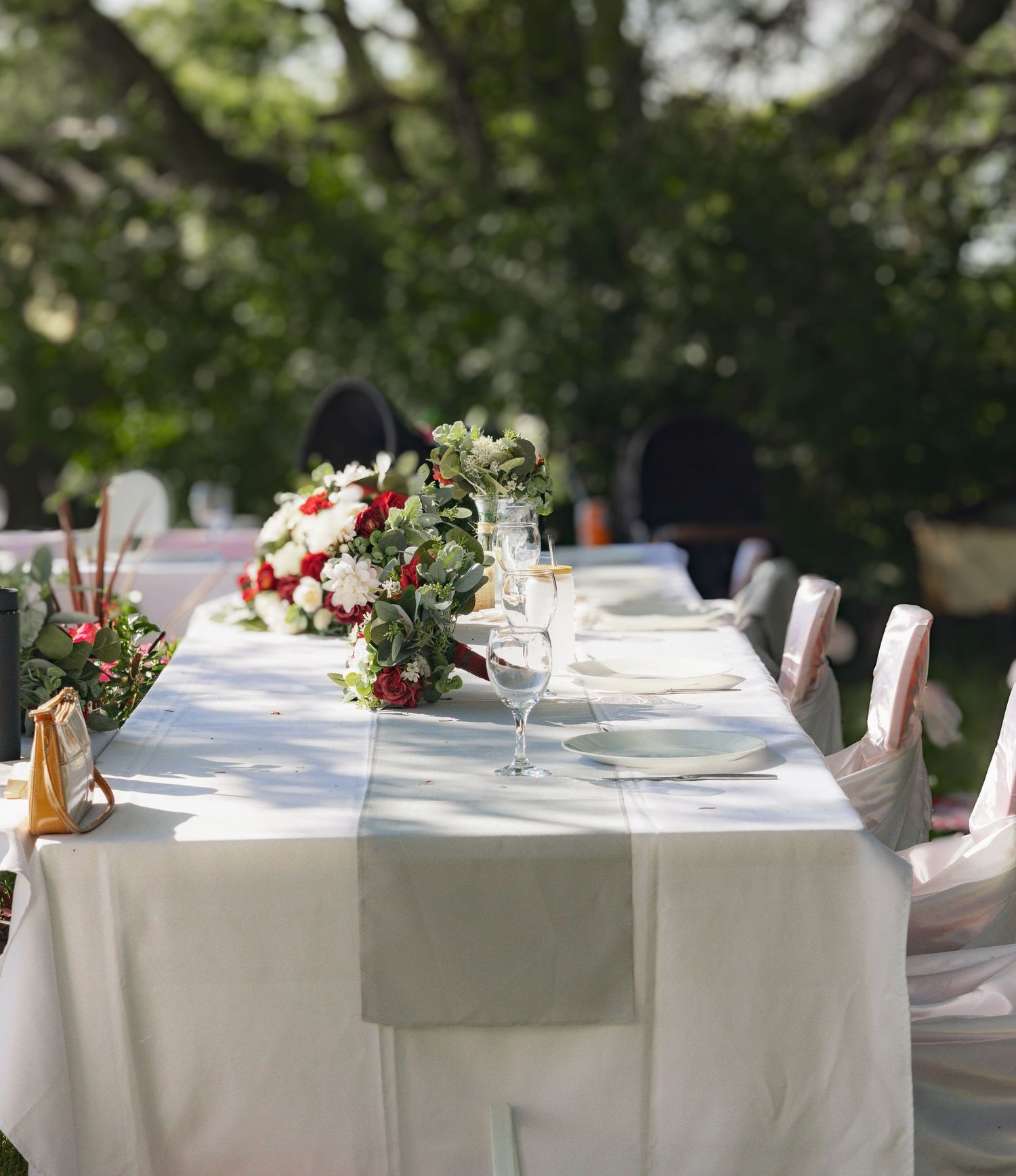 Elegant wedding reception tables set with white linens and floral centerpieces in an outdoor setting.