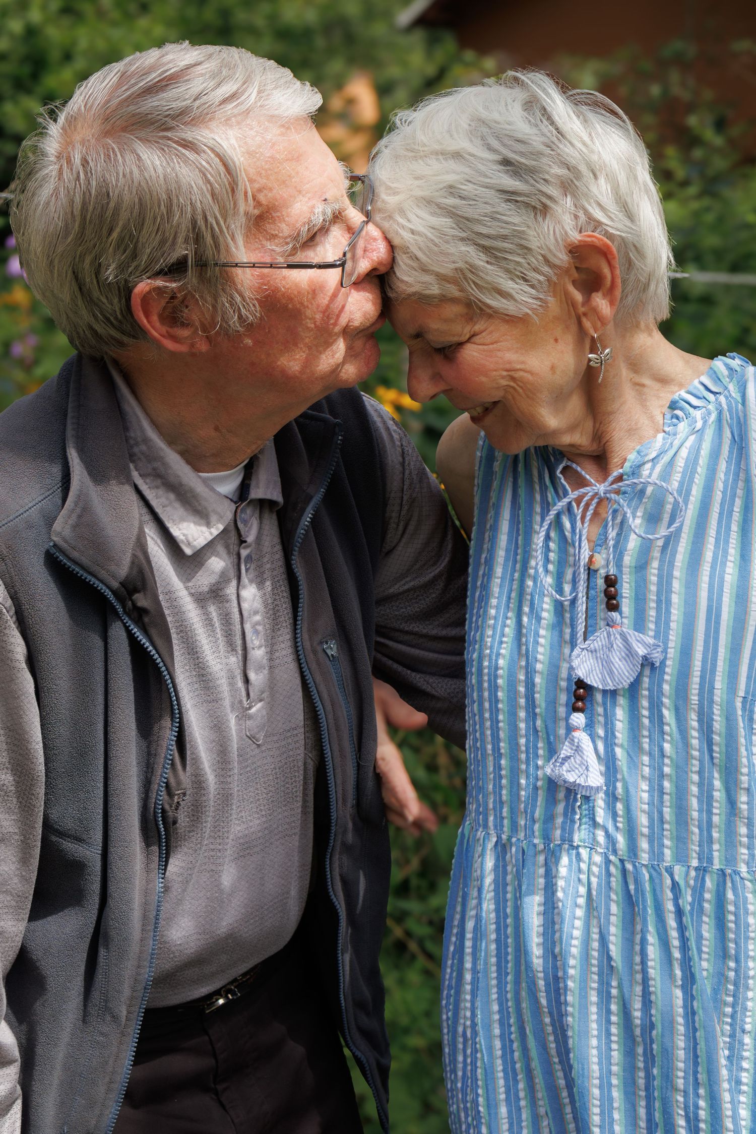 Elderly couple in casual attire share an intimate moment on a bench.