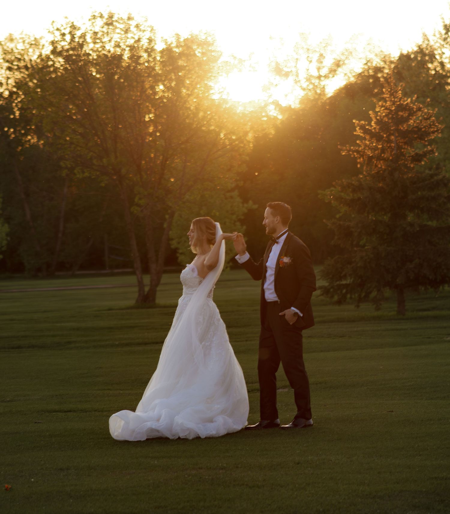 Bride and groom walking together in a park during a dramatic sunset.