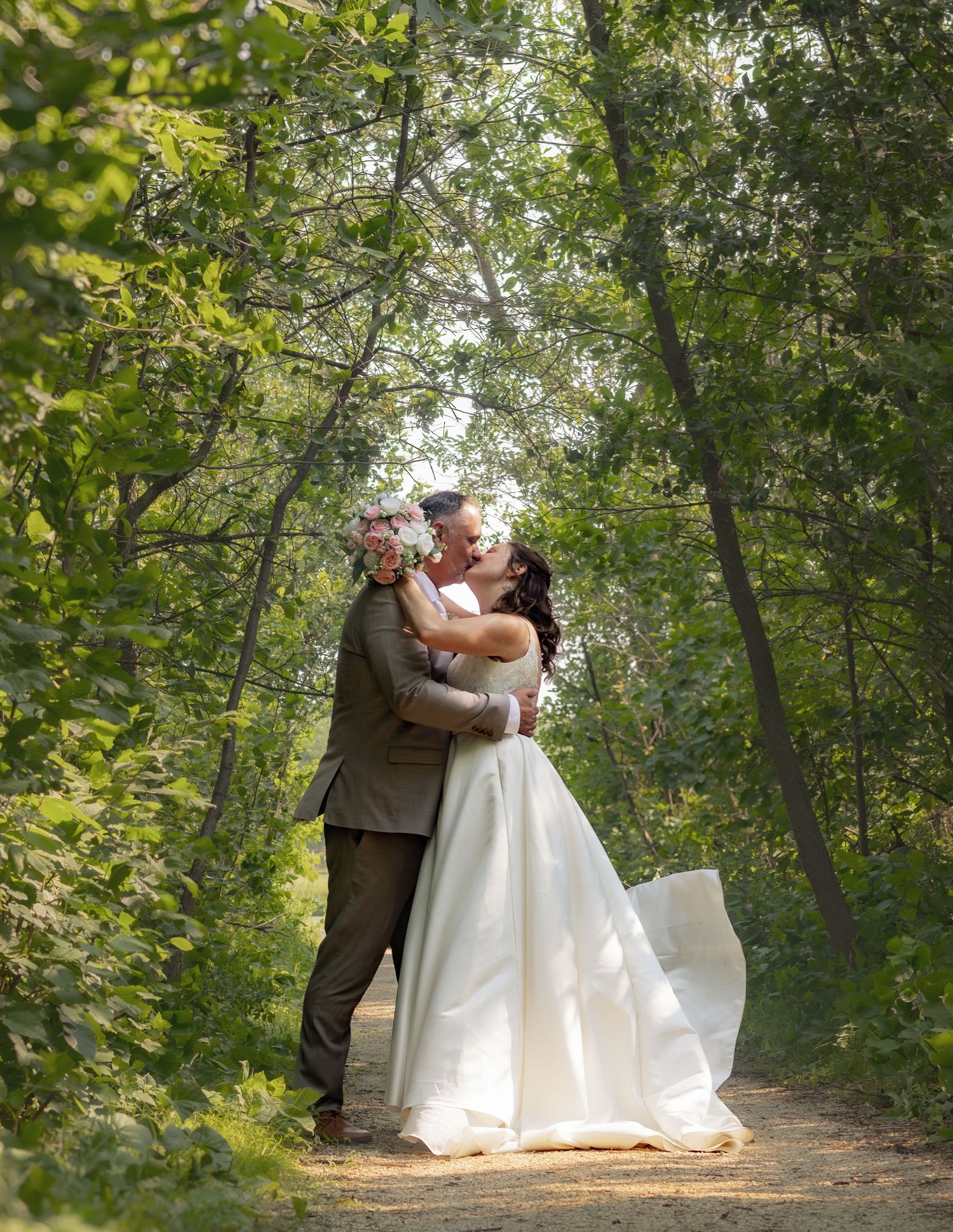 A couple shares their first dance on a tree-lined path during their wedding celebration.
