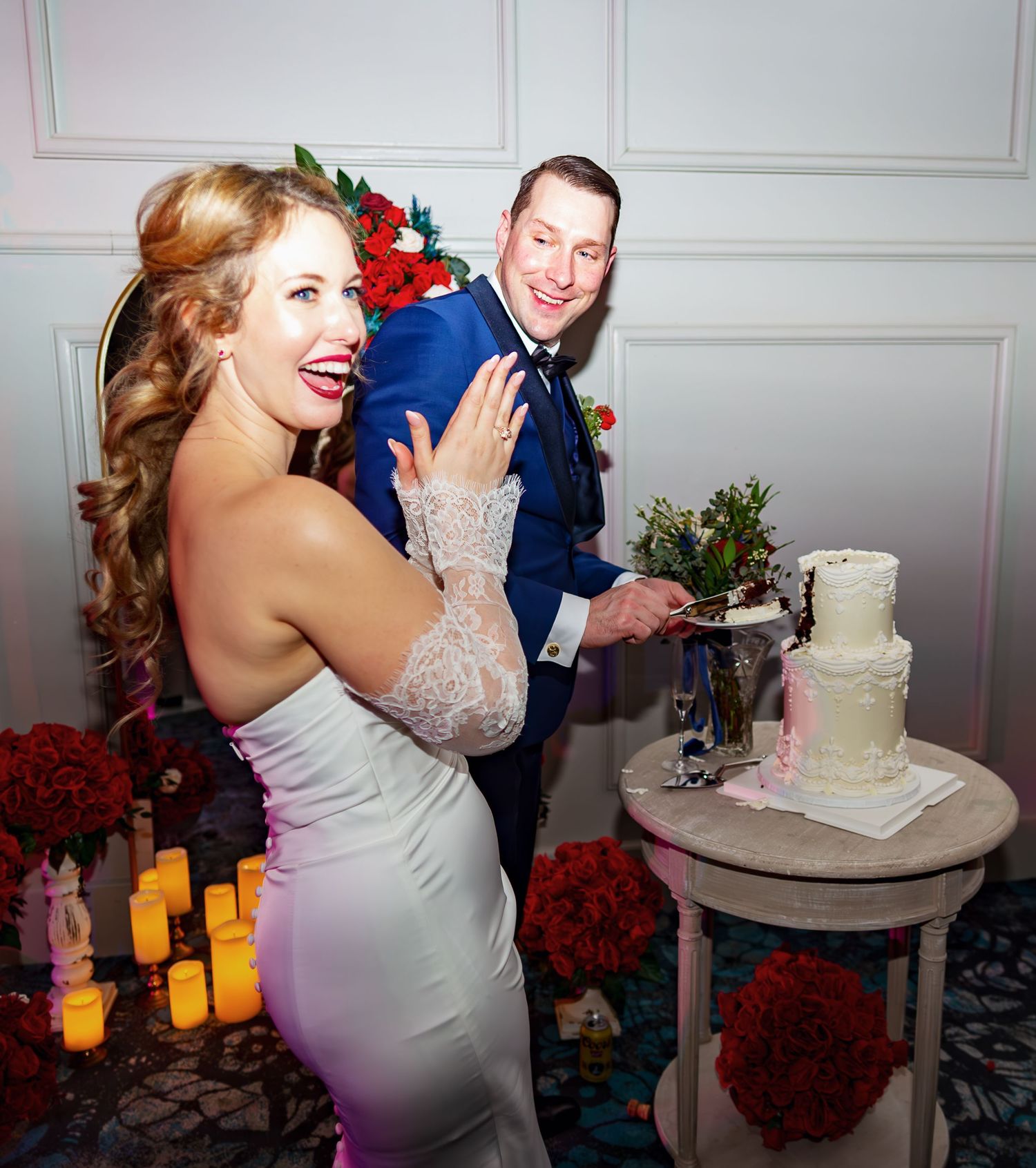 Wedding cake cutting moment captured at an elegant reception with red floral decor.