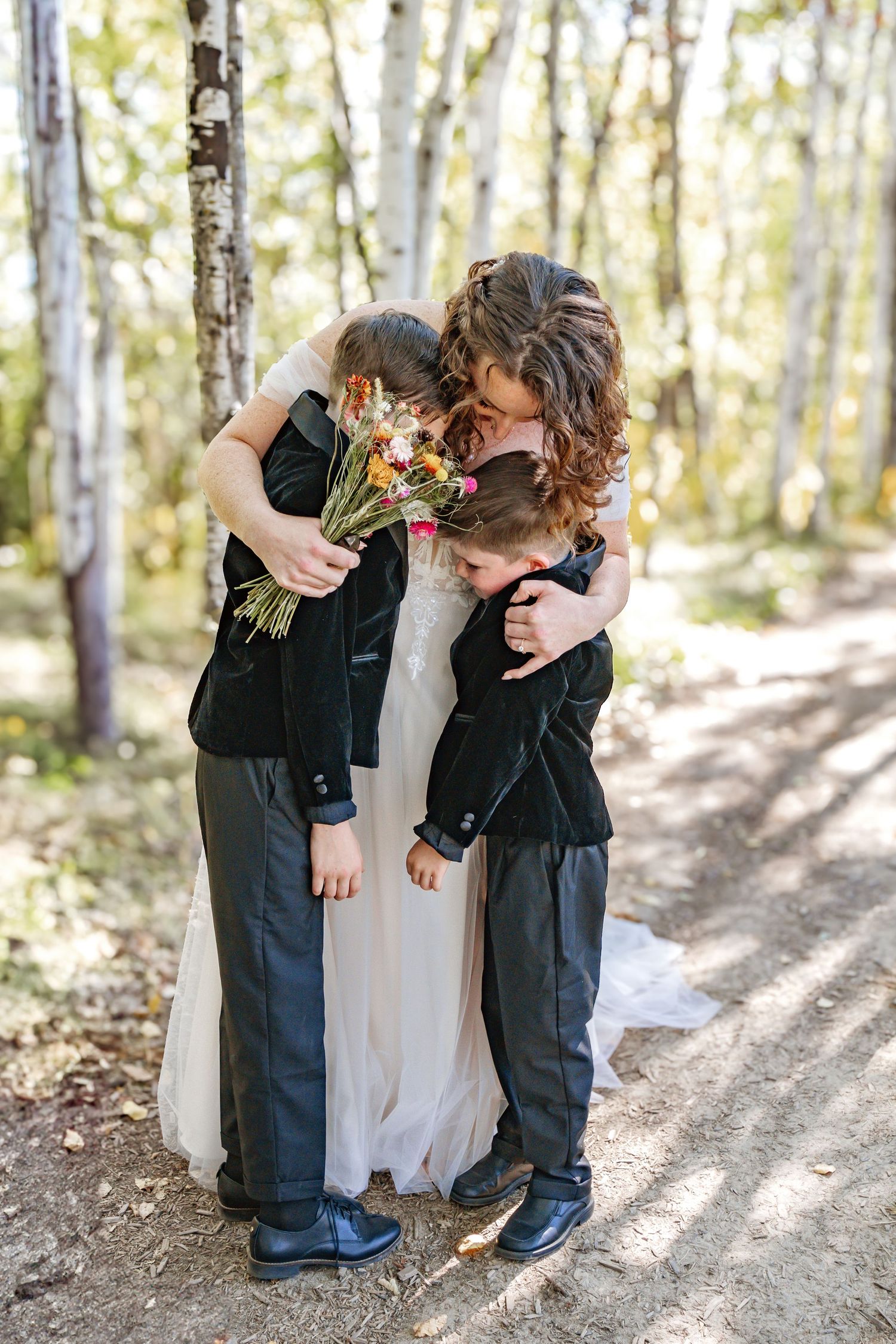 Young ring bearers in dark suits bowing playfully next to a white wedding dress.
