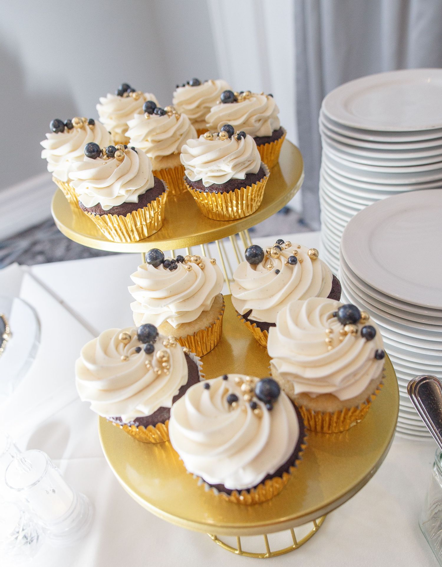 Elegant white frosted cupcakes with blueberries displayed on gold stands at a wedding dessert table.