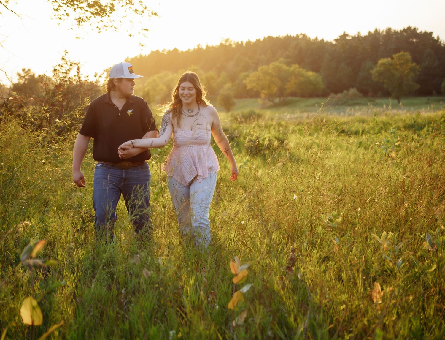 Couple walking through a sunlit meadow during golden hour.