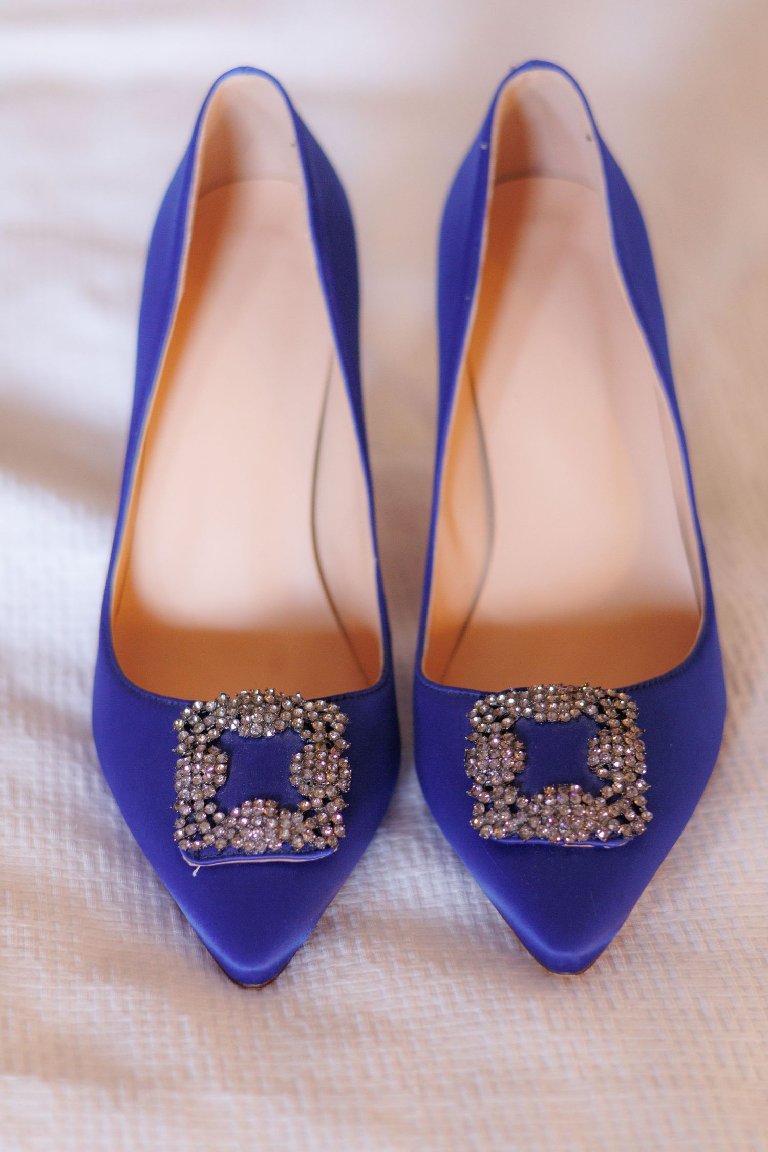 Royal blue pointed-toe flats with crystal embellished buckles on white fabric.