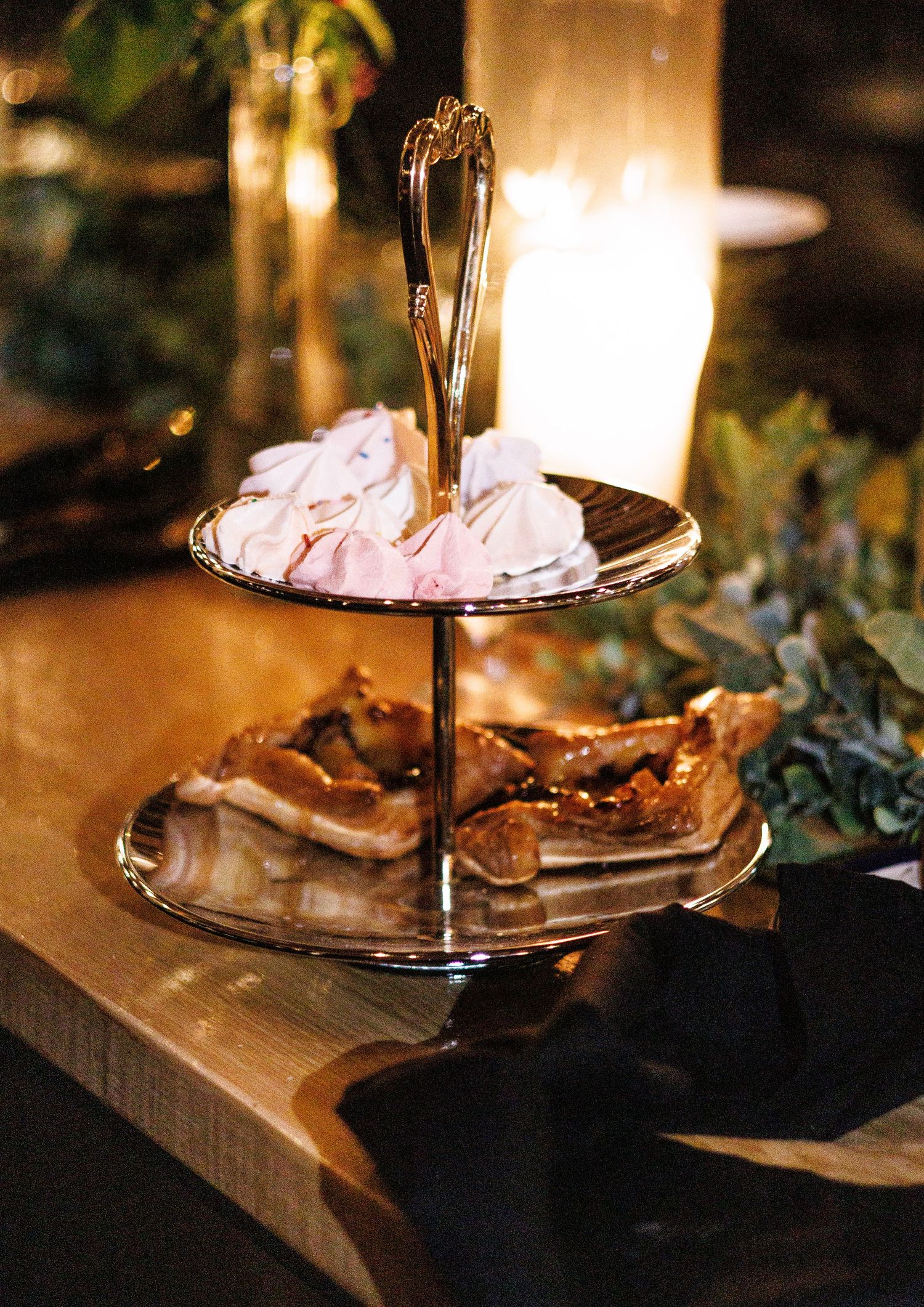 Wedding cake display on wooden table with ambient lighting and greenery decorations.