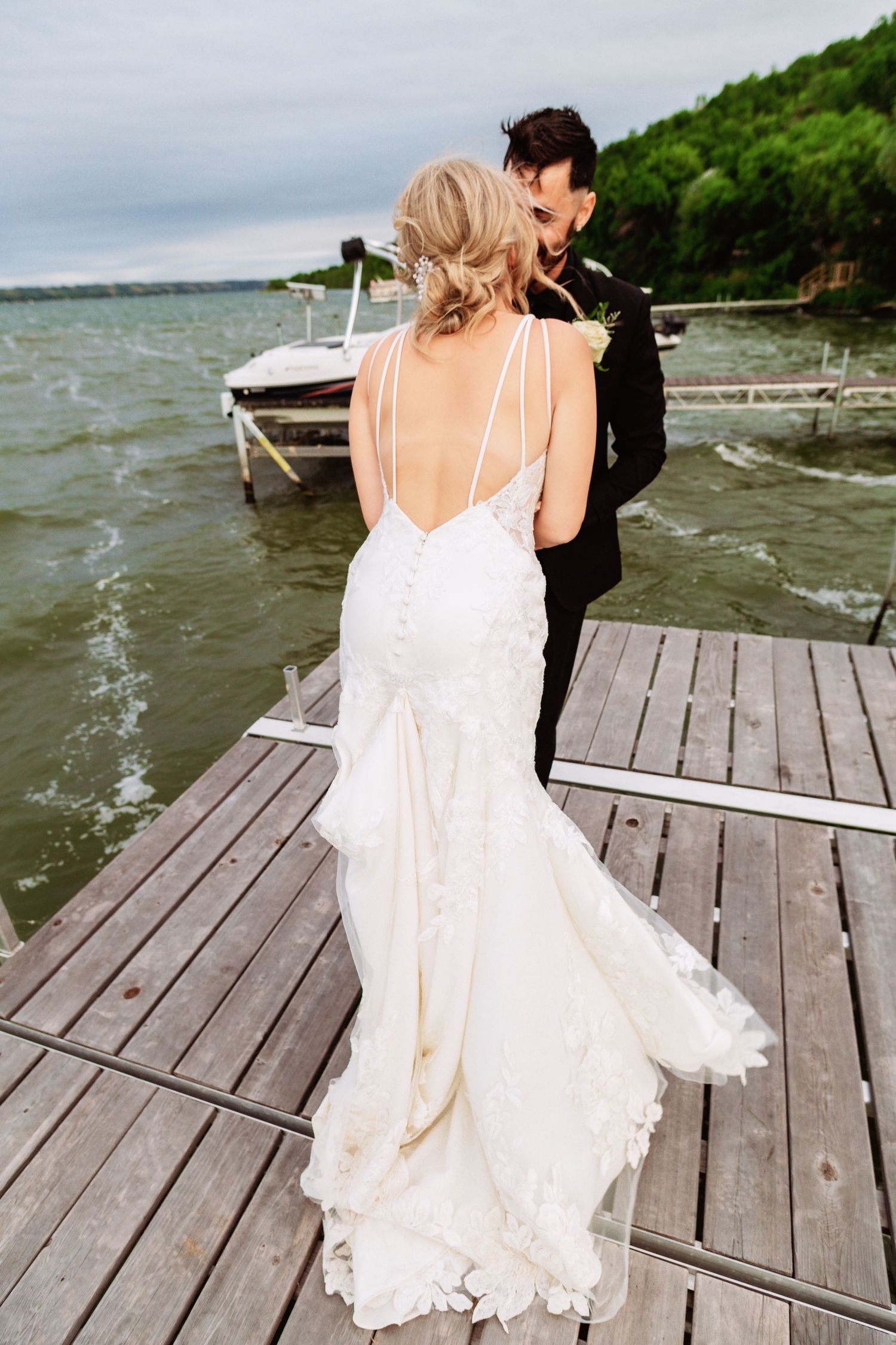 Romantic moments captured on a lakeside dock during a windy wedding photoshoot.