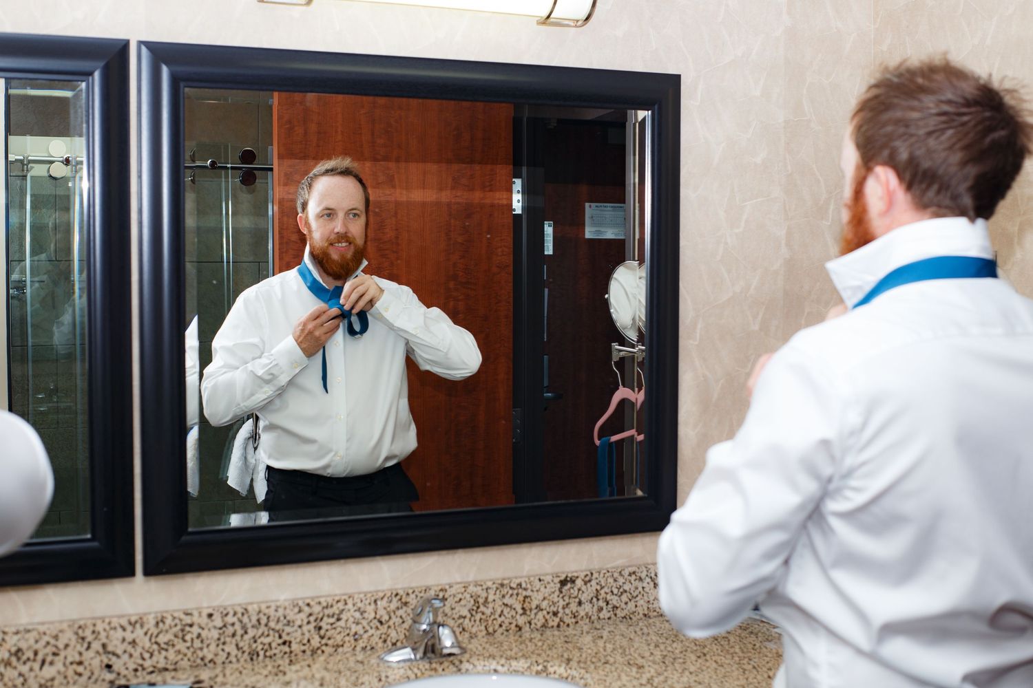Mirror reflection of person adjusting tie while getting ready.