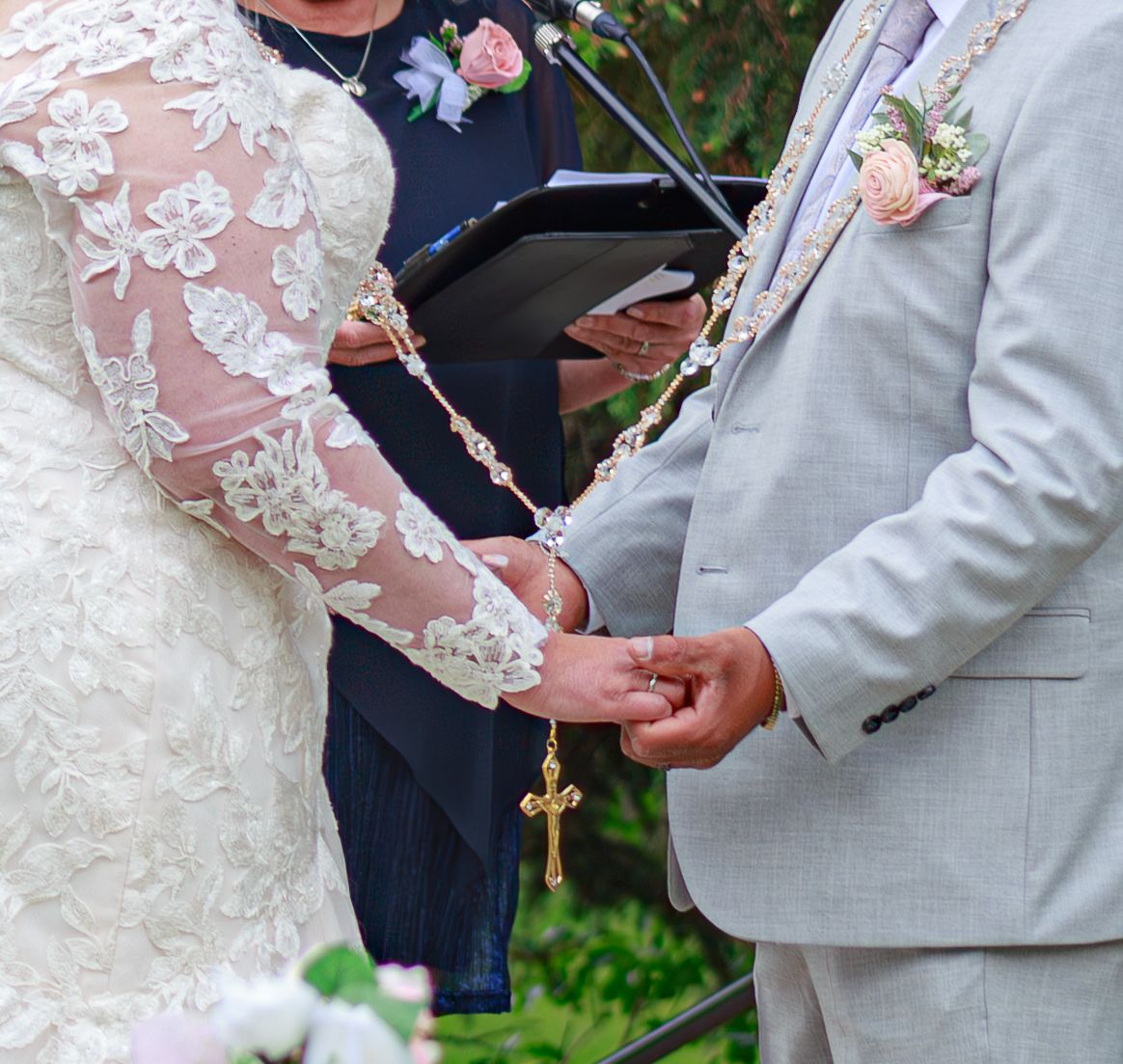Close-up of hands during a wedding ceremony with lace details and a decorative cross.
