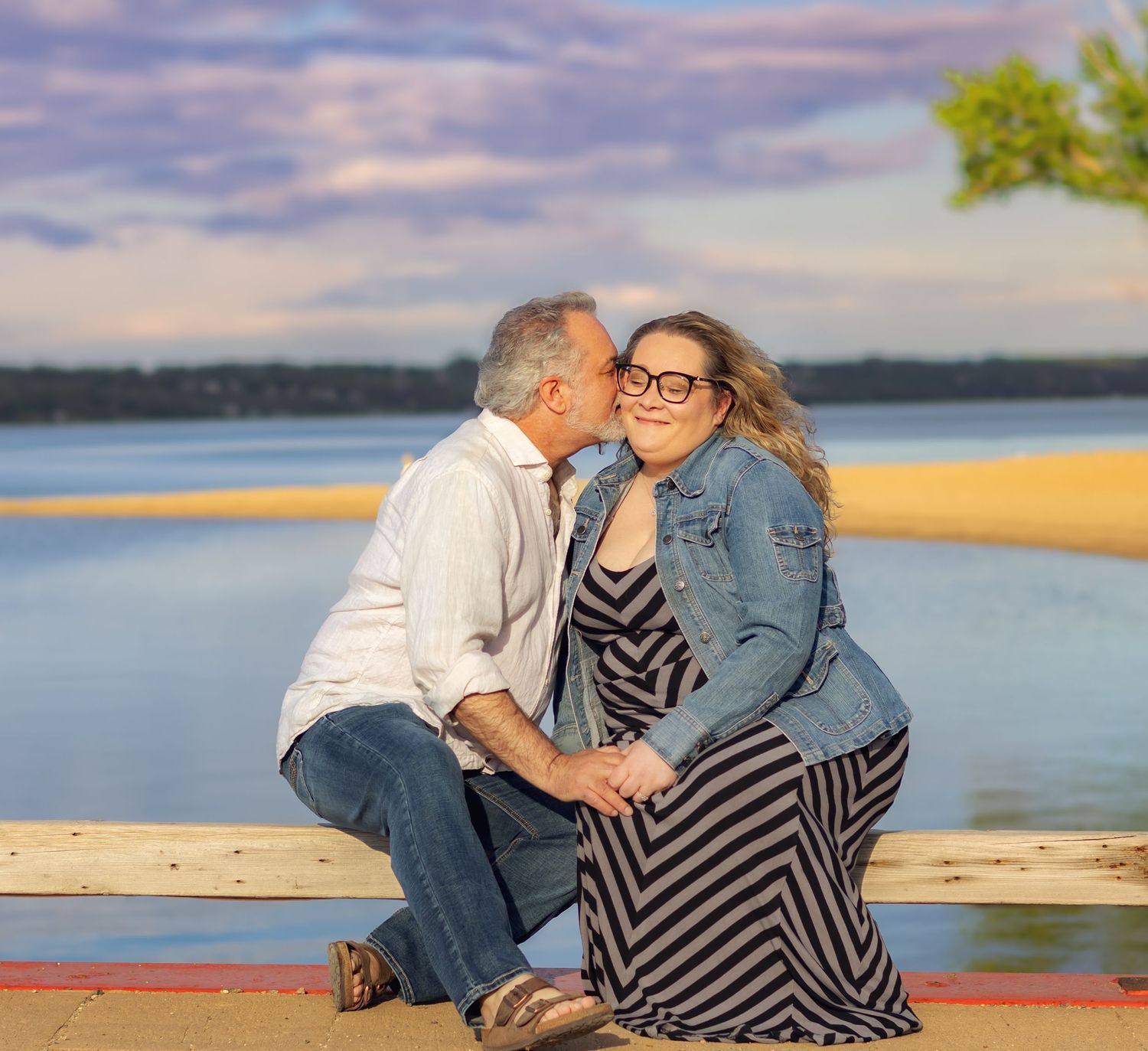 Couple sharing intimate moment on wooden dock by lake during sunset.