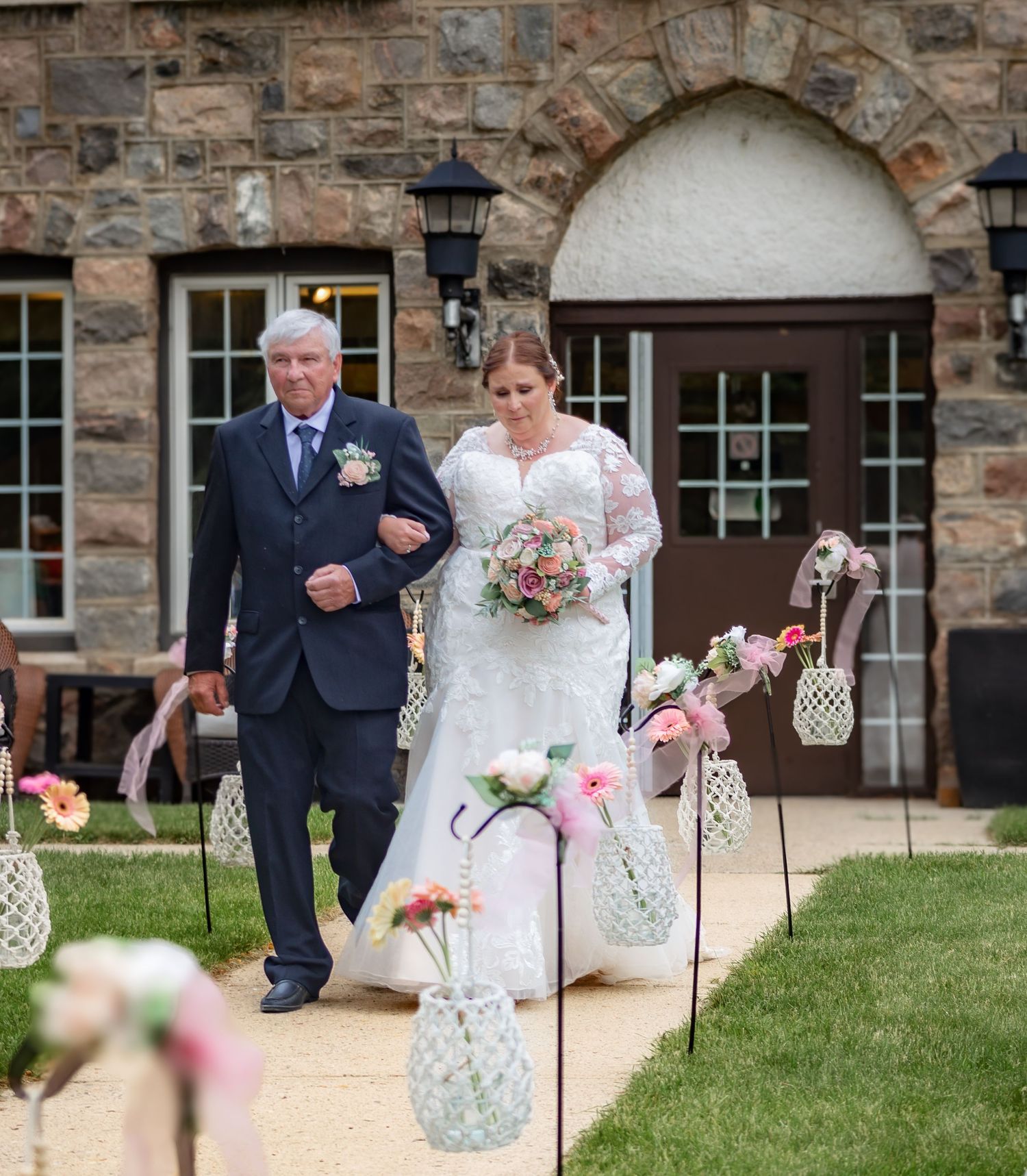 Wedding ceremony setup with lantern decorations along stone building pathway.