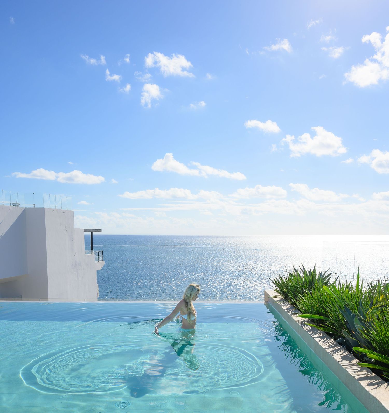 Crystal clear infinity pool with rippling water against bright blue sky.