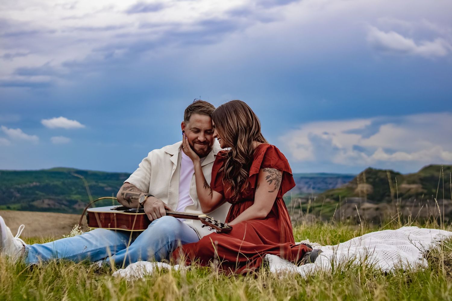 Couple enjoying a picnic on a grassy hilltop with dramatic cloudy sky backdrop.