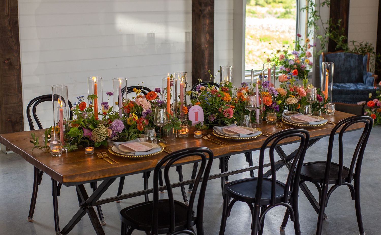 Rustic wedding reception setup with wooden tables and chairs decorated with floral arrangements and place settings.