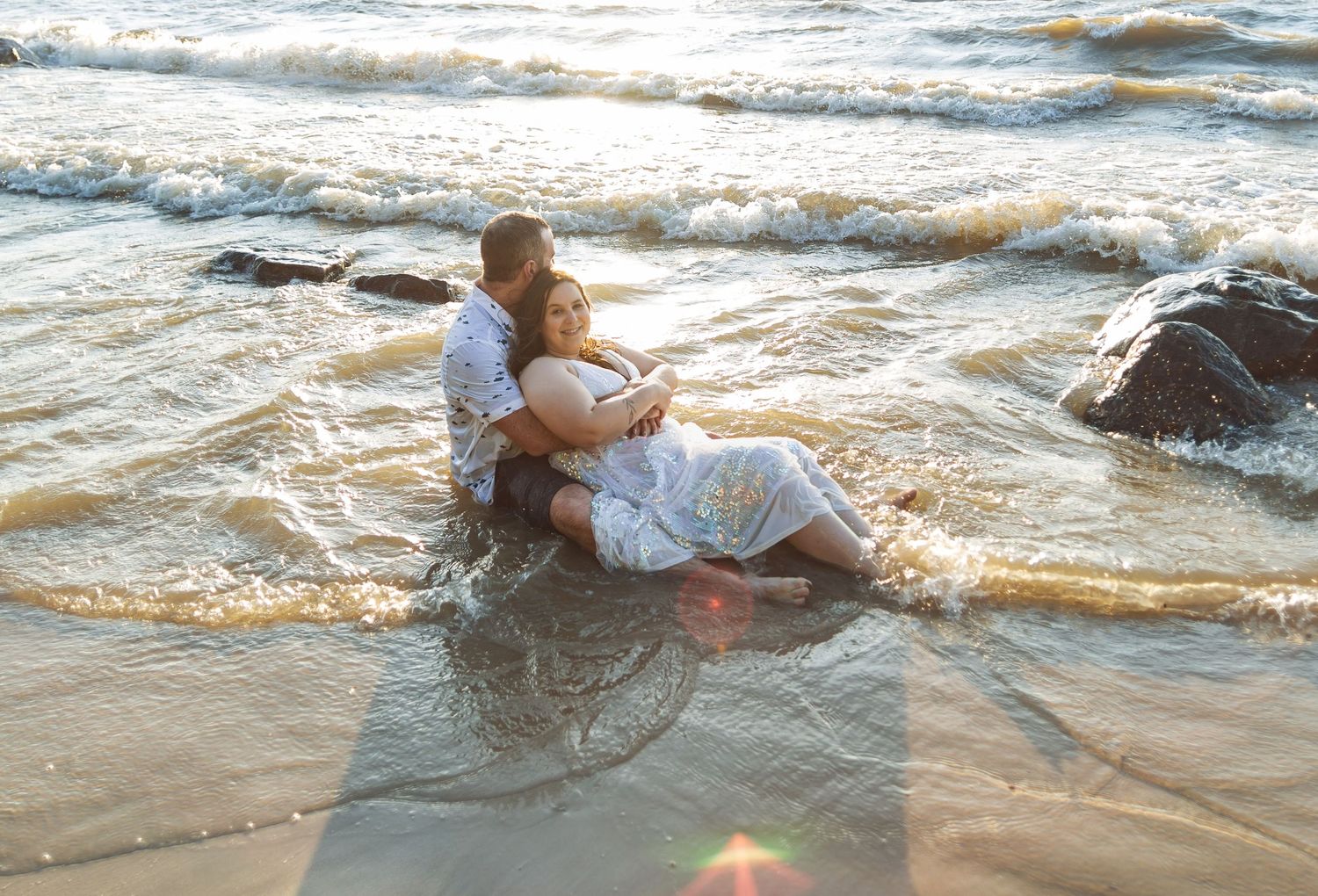 A couple shares a romantic moment on rocky beach at sunset.