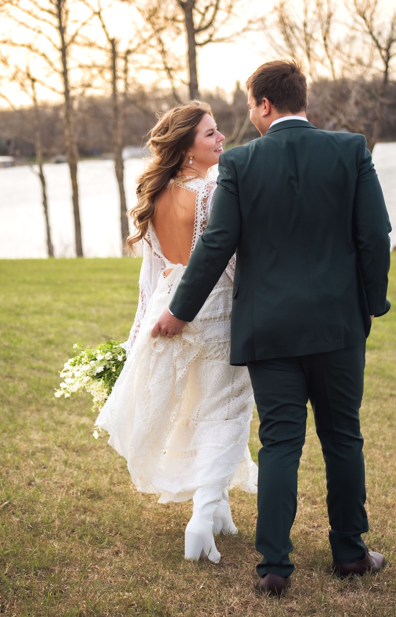 A couple walks hand in hand through a scenic lakeside park during their wedding.