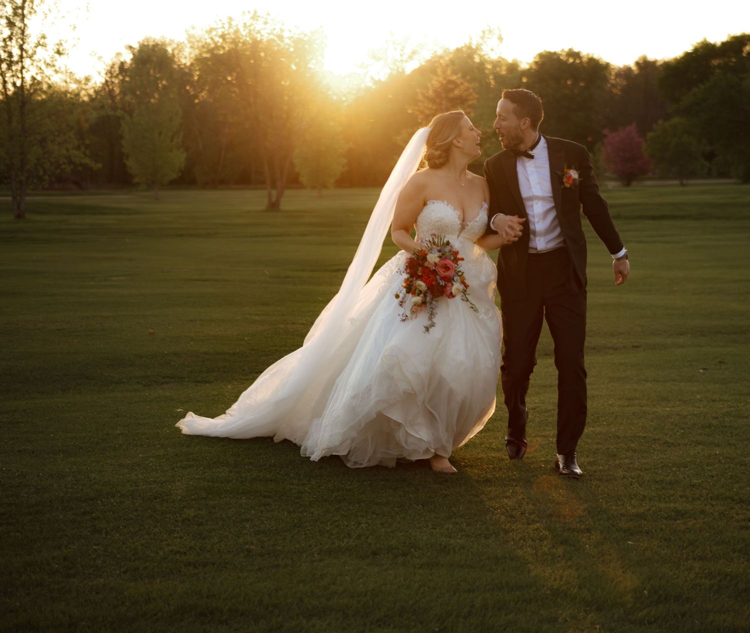 Wedding couple walking through a golden sunset field in formal attire.