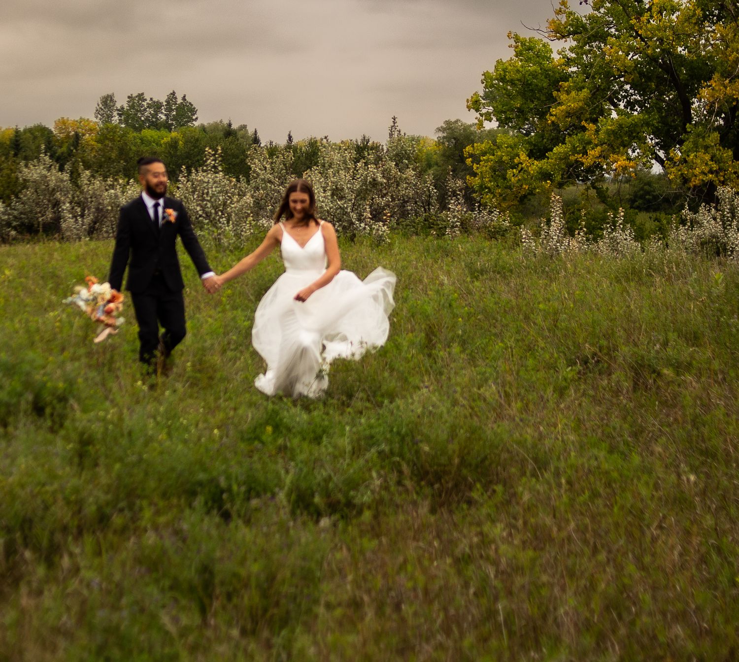 Wedding couple walking through tall grass in a natural outdoor setting.