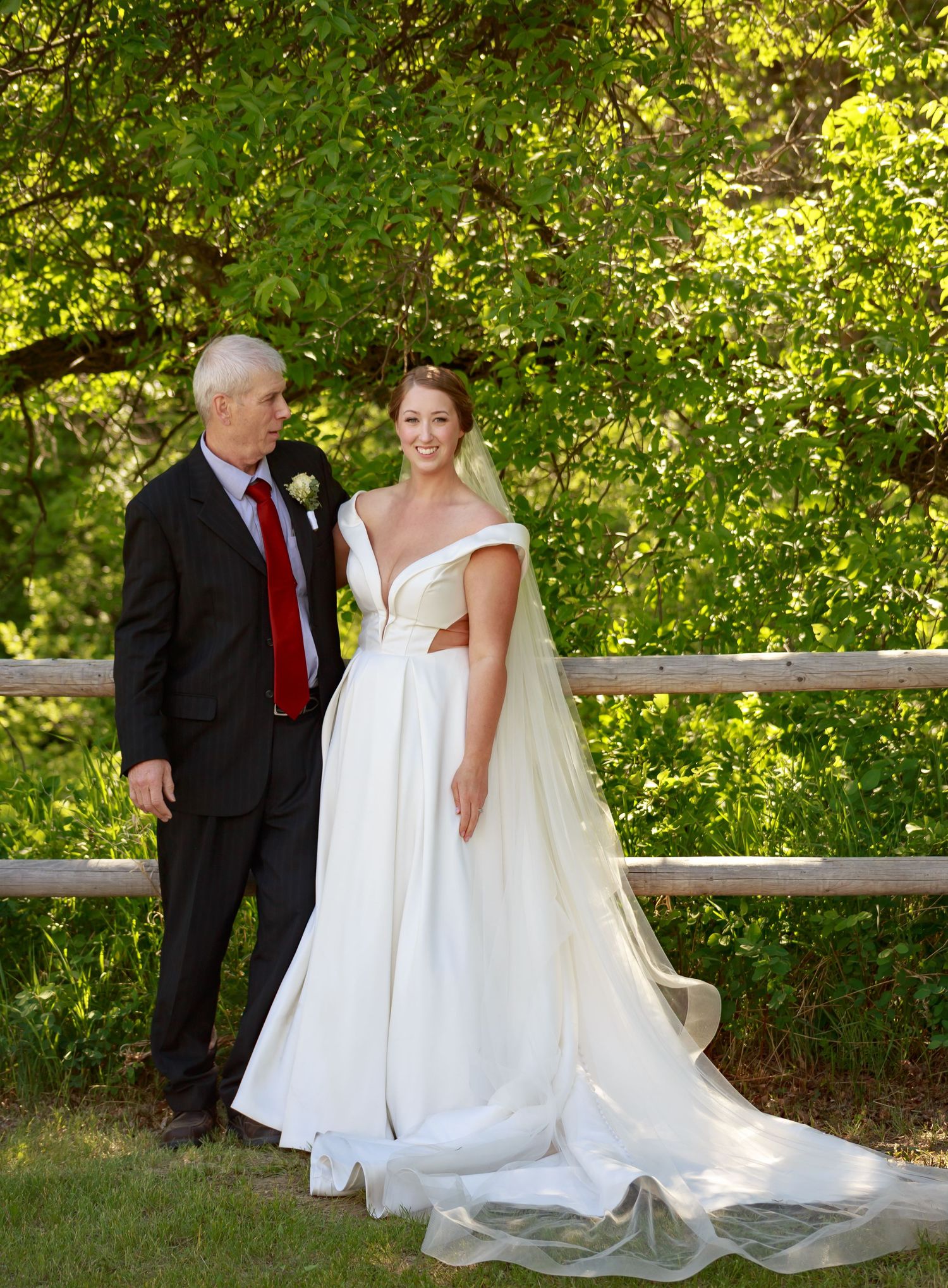 Wedding party gathered on wooden deck with lush green foliage background.
