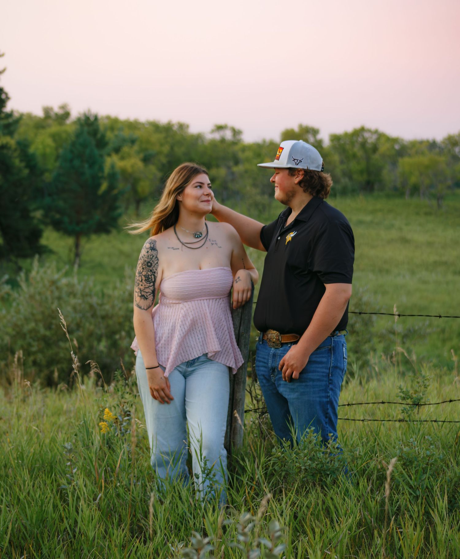 Couple enjoying each other's company by a rustic fence in a green meadow.